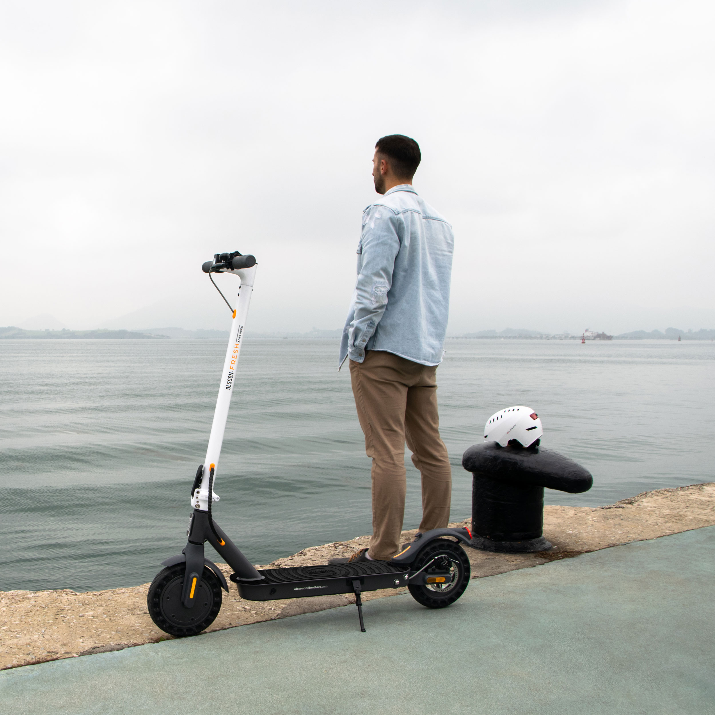 Mann neben einem Elektroroller auf einem Pier. Ozean im Hintergrund. Bewölkter Himmel.