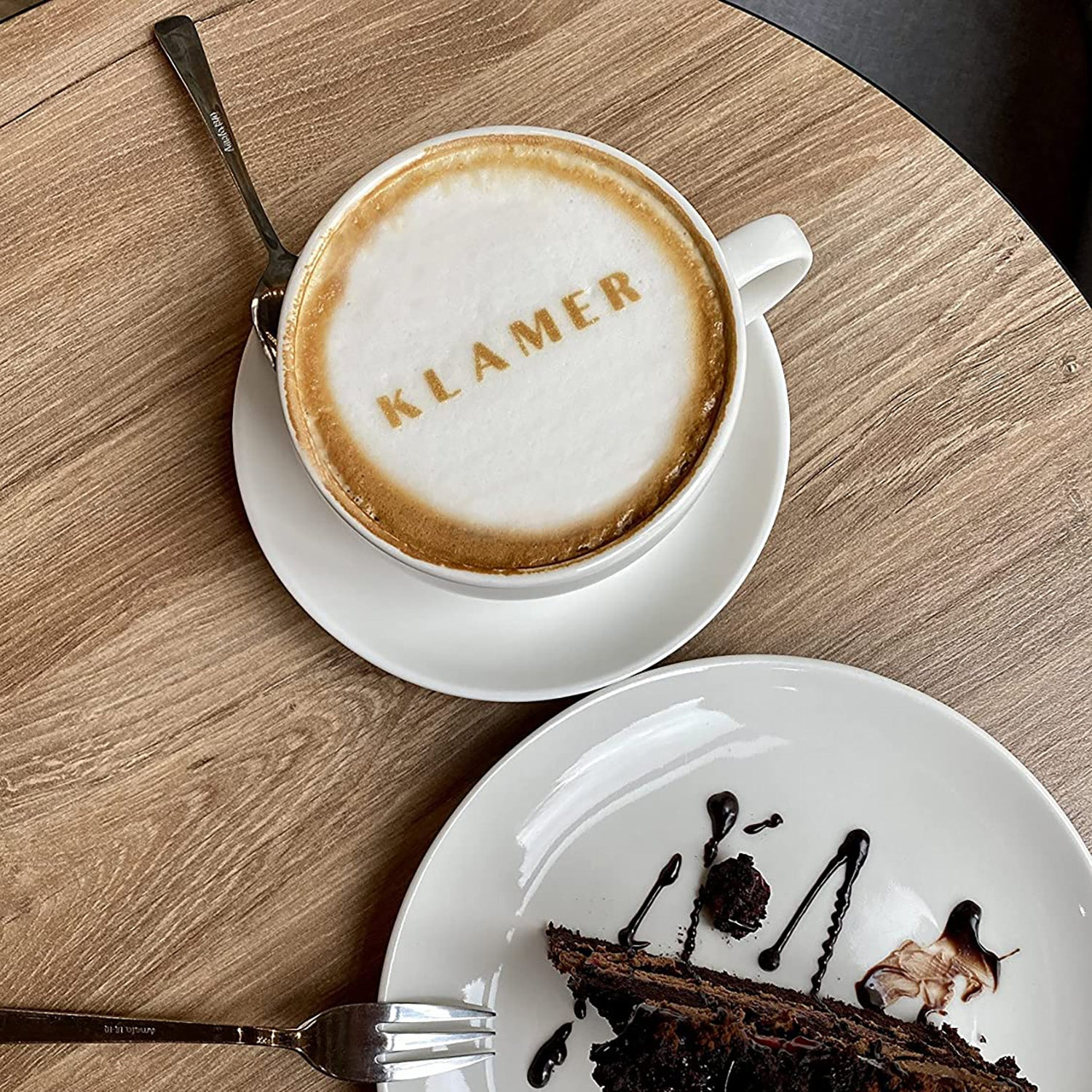Kaffee mit KLAMER auf dem Schaum, serviert mit Kuchen auf einem weißen Teller.