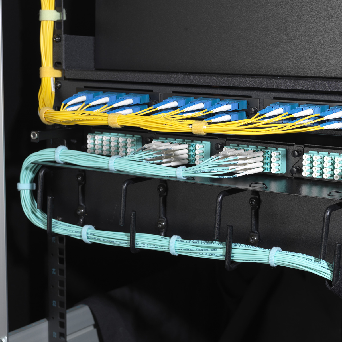 Server-Rack voller Kabel. Blaue, gelbe und grüne Kabel. Schwarze Haken. Weißer Hintergrund.
