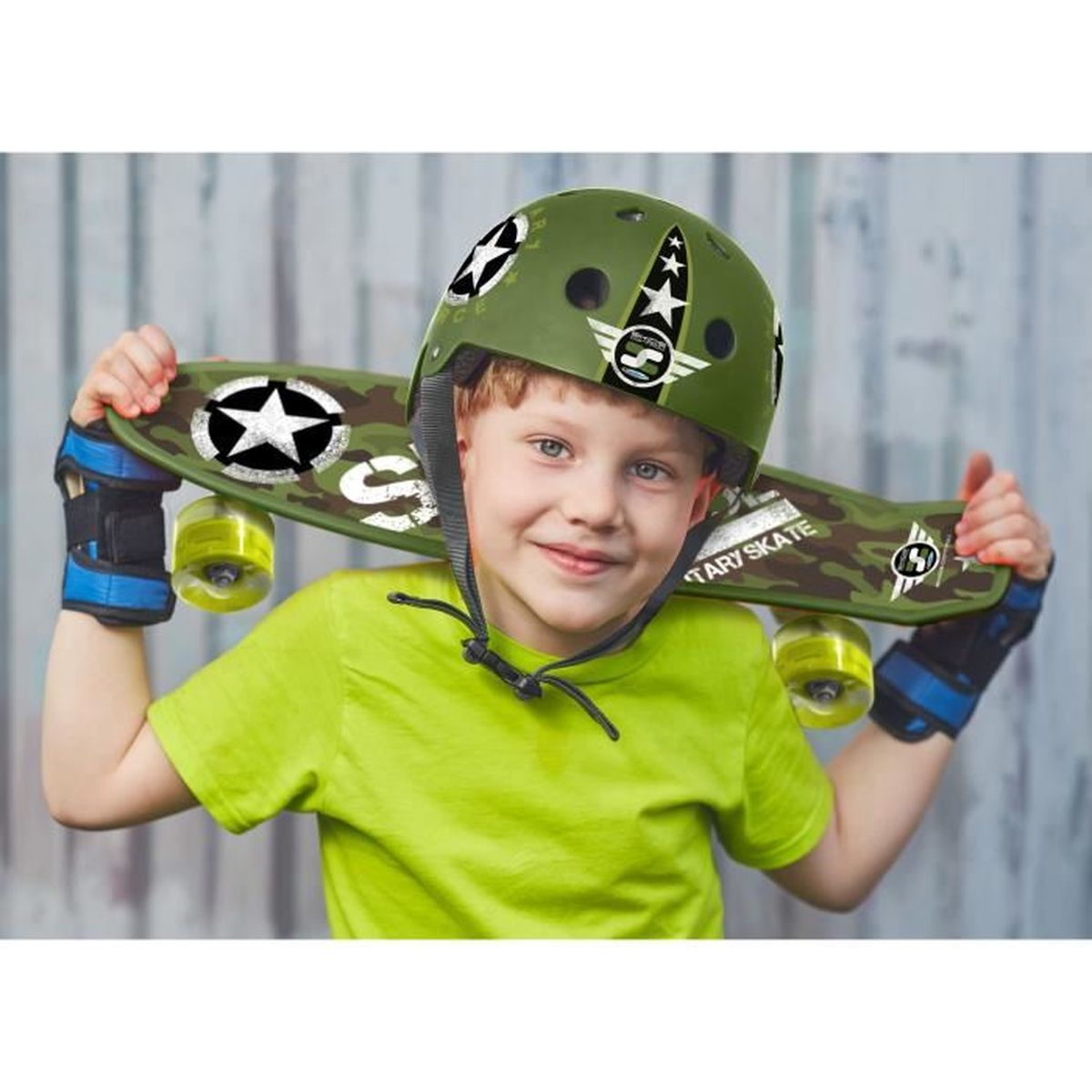 Un jeune garçon portant un casque et un skateboard verts, tenant la planche, souriant à la caméra.