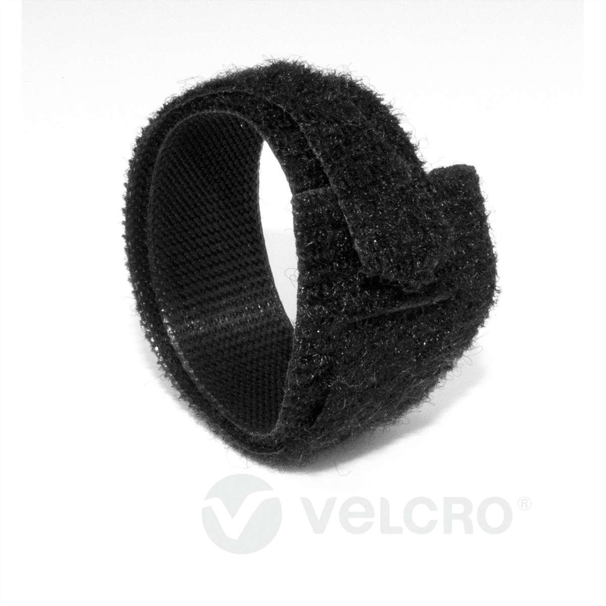 Un cinturino in velcro nero arrotolato in un anello, su sfondo bianco. Il logo 'Velcro' in basso.