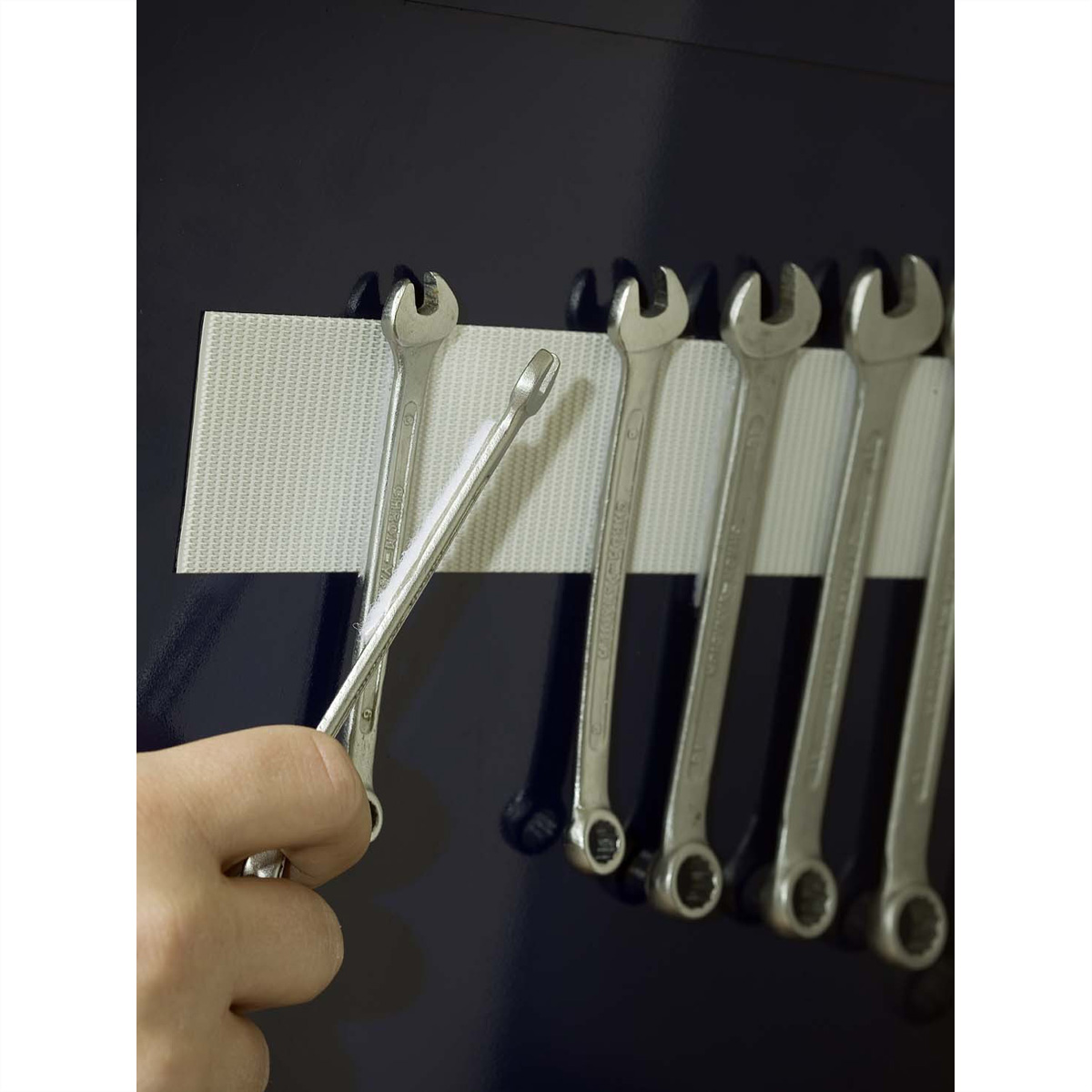 Hand verwijdert een moersleutel van een magnetische gereedschapshouder.