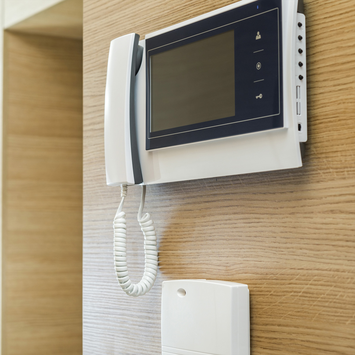 Wit intercomsysteem gemonteerd op een met hout beklede muur, met een handset en kleine knop.