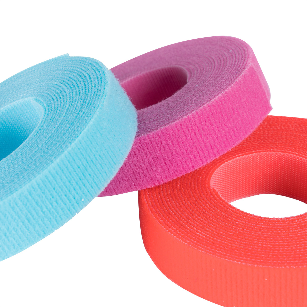Tre rotoli di cinghie in velcro. Rosa, blu e rosso. Il velcro è avvolto su se stesso.