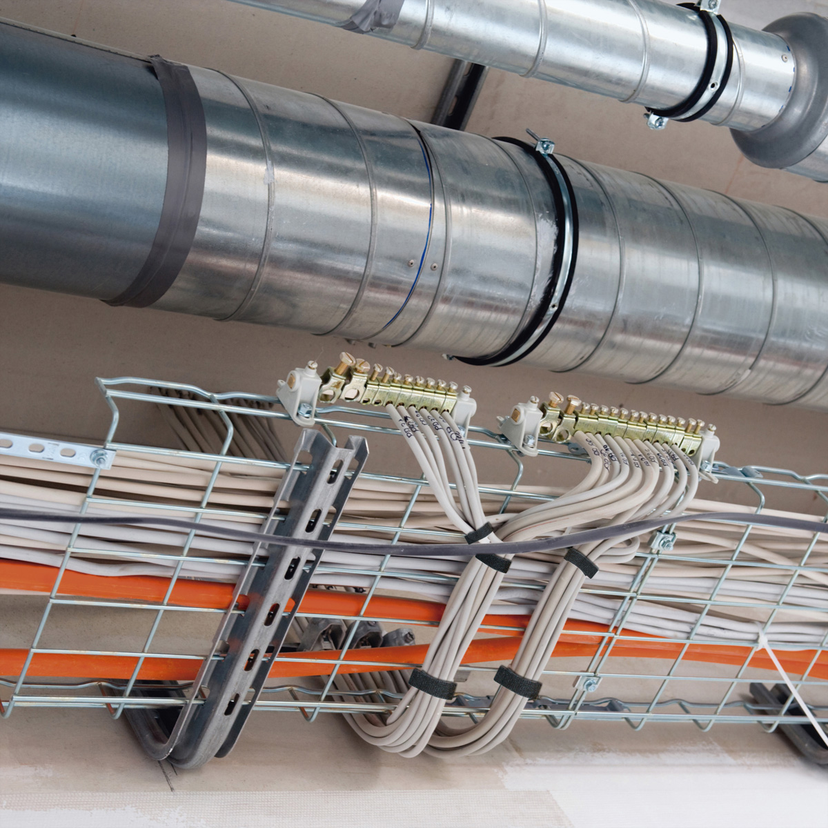 Cavi e condotti metallici sul soffitto, fissati con griglie metalliche e fascette.