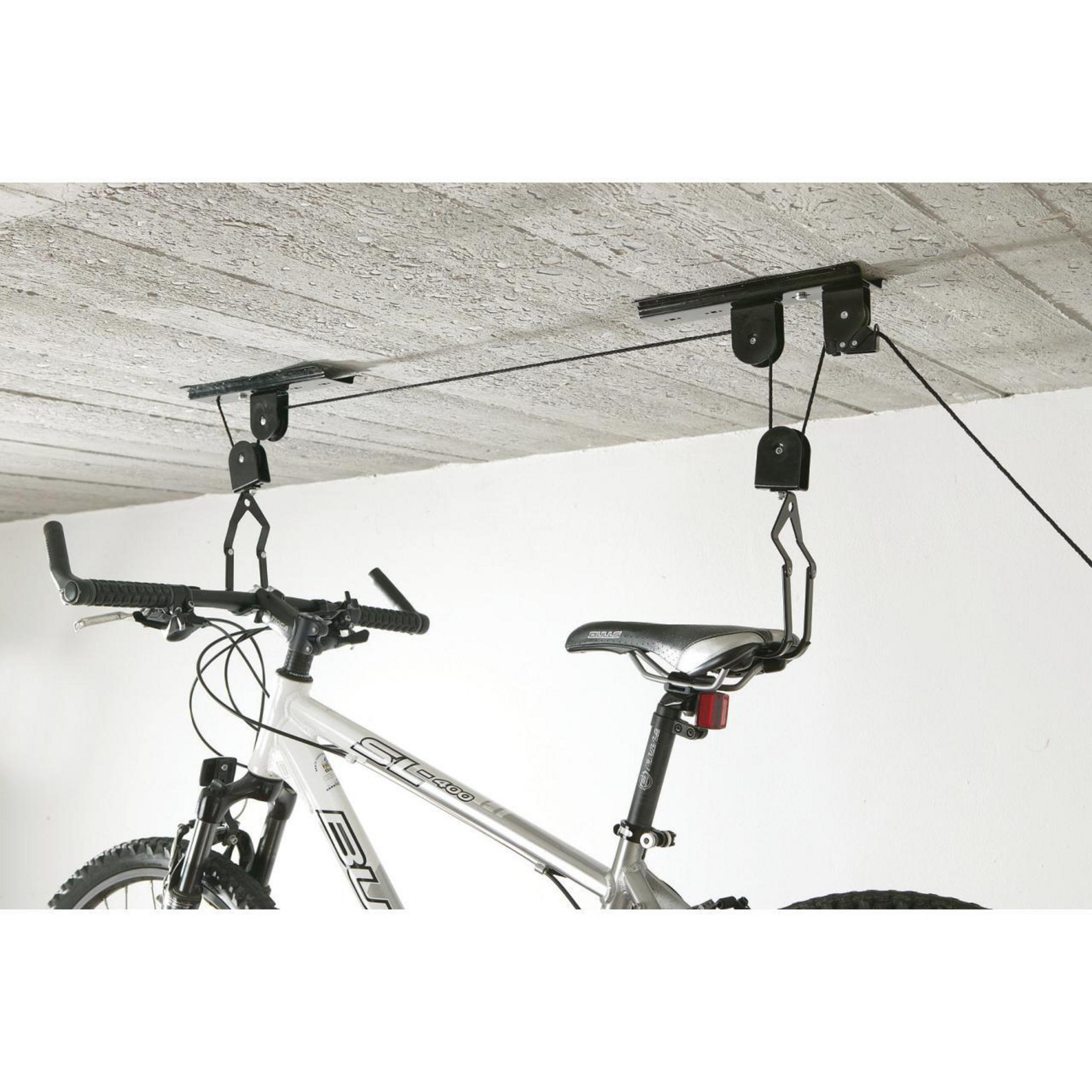 Fahrrad hängt mit Rollen von der Decke. Weißes Fahrrad, schwarze Rollen und graue Decke.