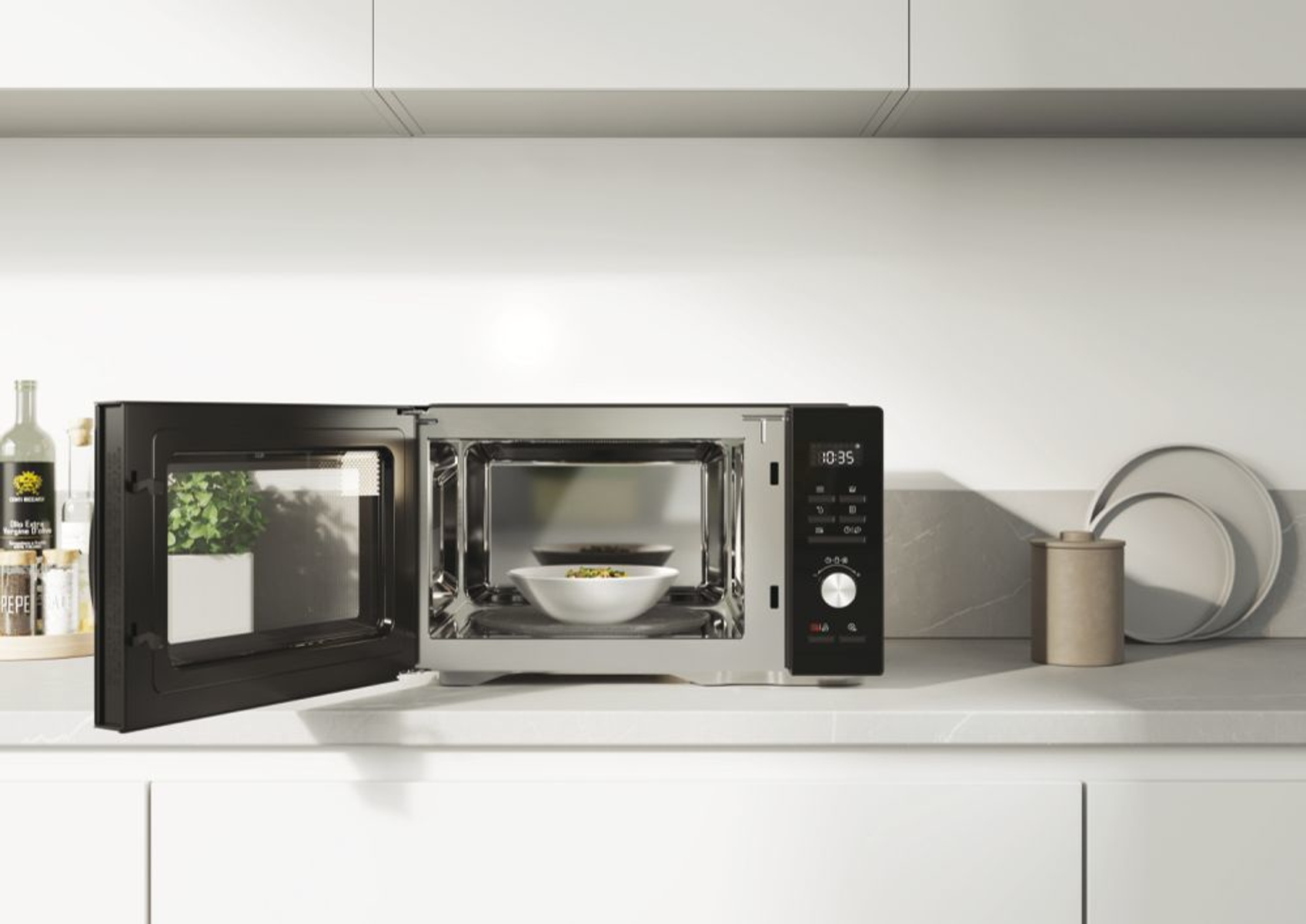 Kuchenka mikrofalowa z otwartymi drzwiami, pokazująca białą miskę z jedzeniem w środku. Blat jest biały.