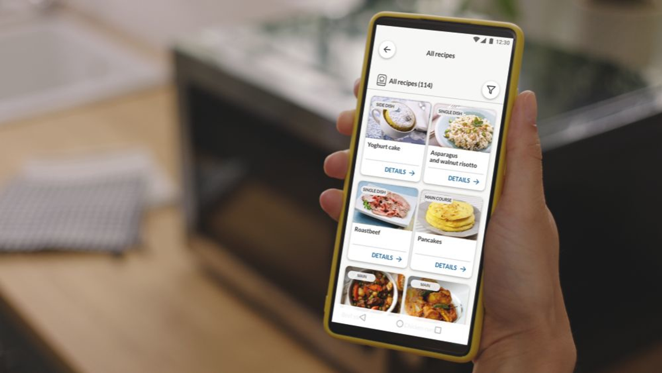 Smartfon wyświetlający aplikację z przepisami. Pokazuje zdjęcia jedzenia i tekst, trzymany w dłoni.