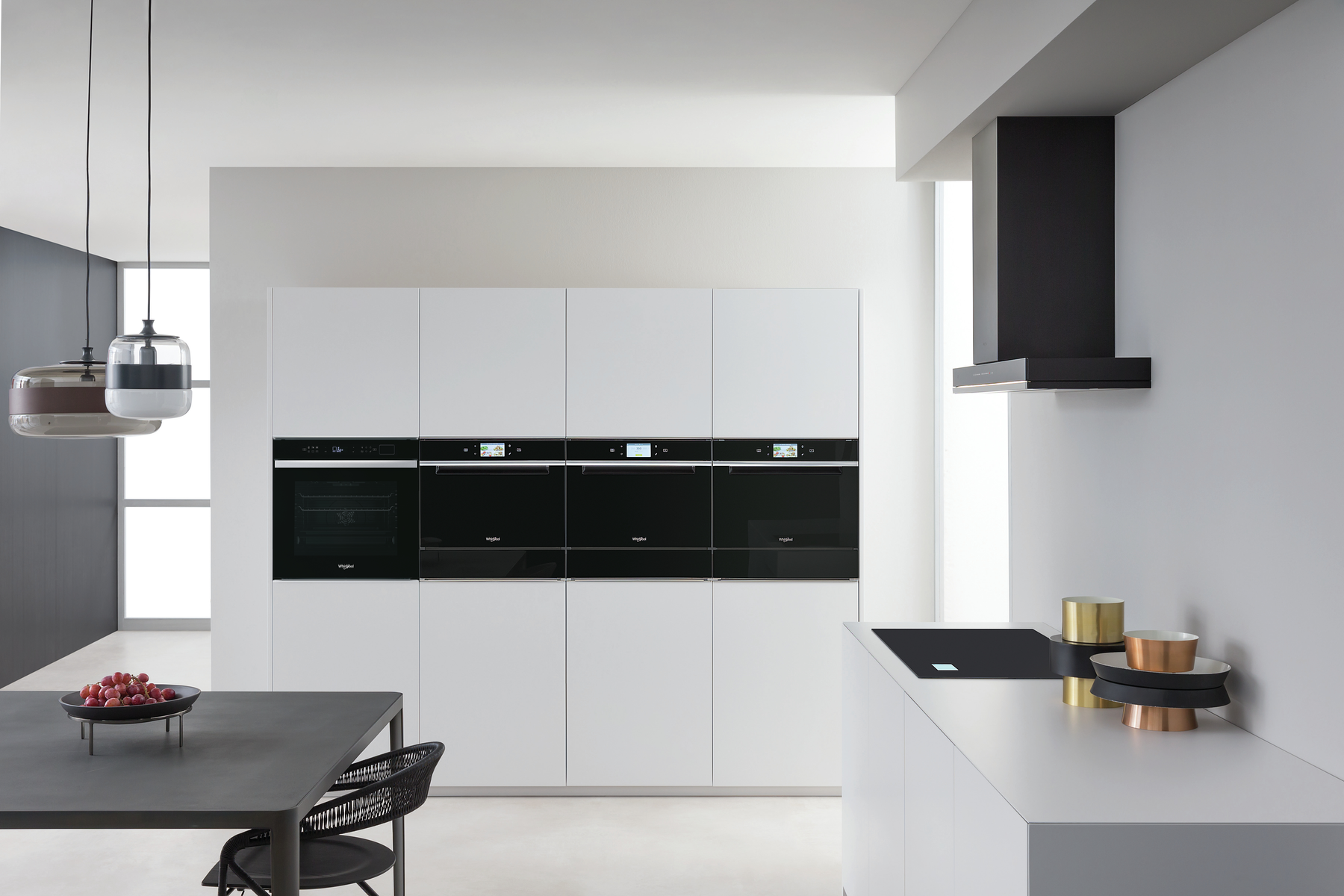 Cocina moderna con hornos empotrados y una encimera negra. Armarios blancos y campana extractora.