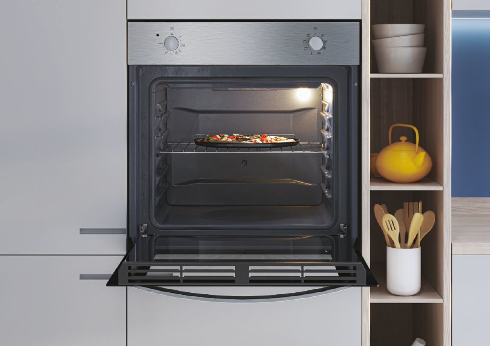 Forno con pizza, porta aperta. Mensole con ciotole, bollitore giallo e utensili.