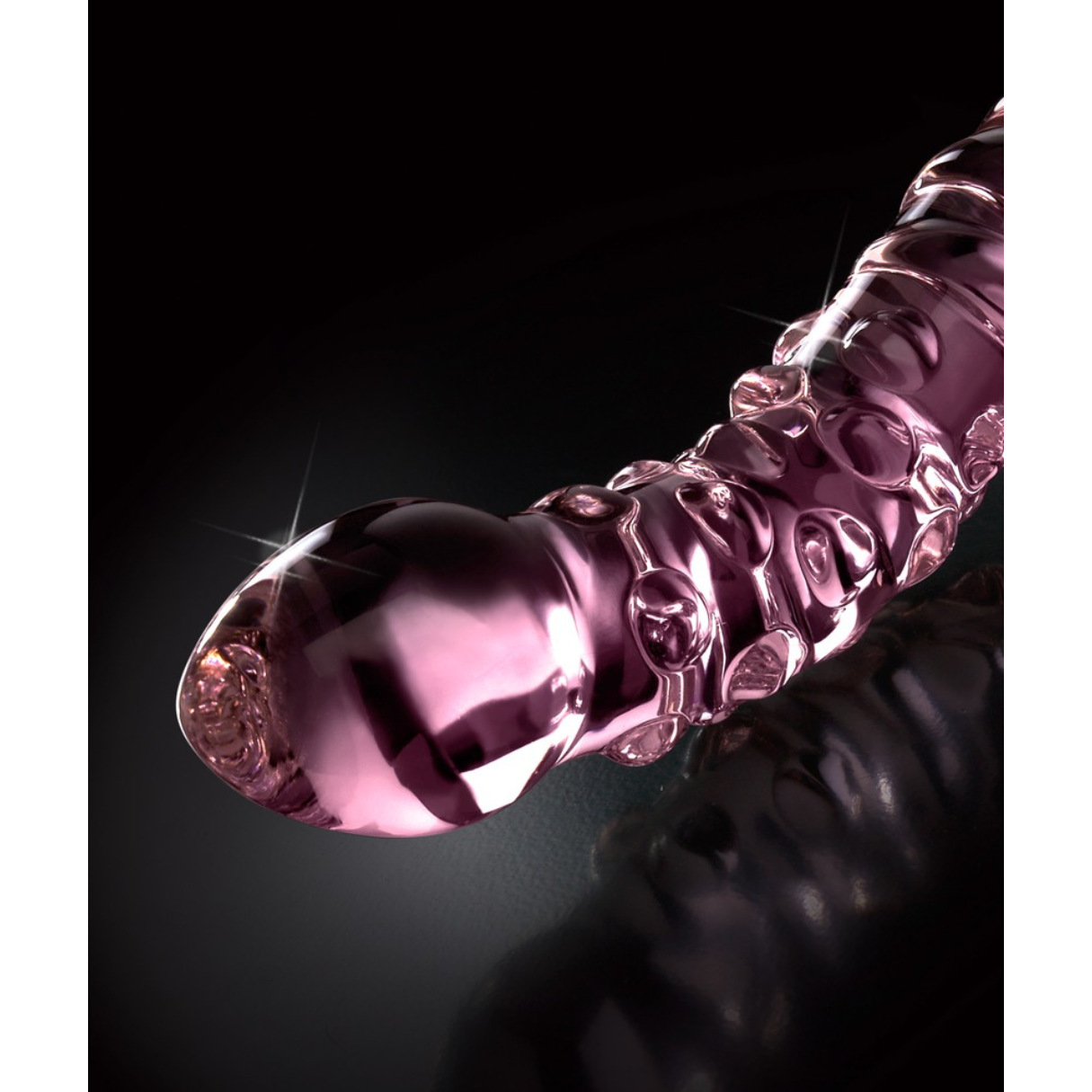 Ein rosa, gerilltes Sexspielzeug auf dunkler Oberfläche, mit einem Scheinwerfer beleuchtet.