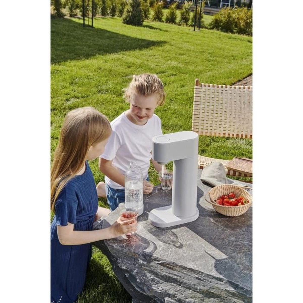 Zwei Mädchen gießen Saft aus einer Flasche an einem Tisch im Garten.