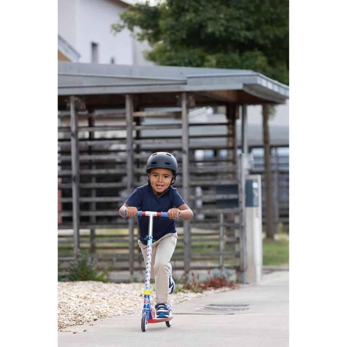 Un bambino con casco guida uno scooter su un marciapiede con struttura in legno.