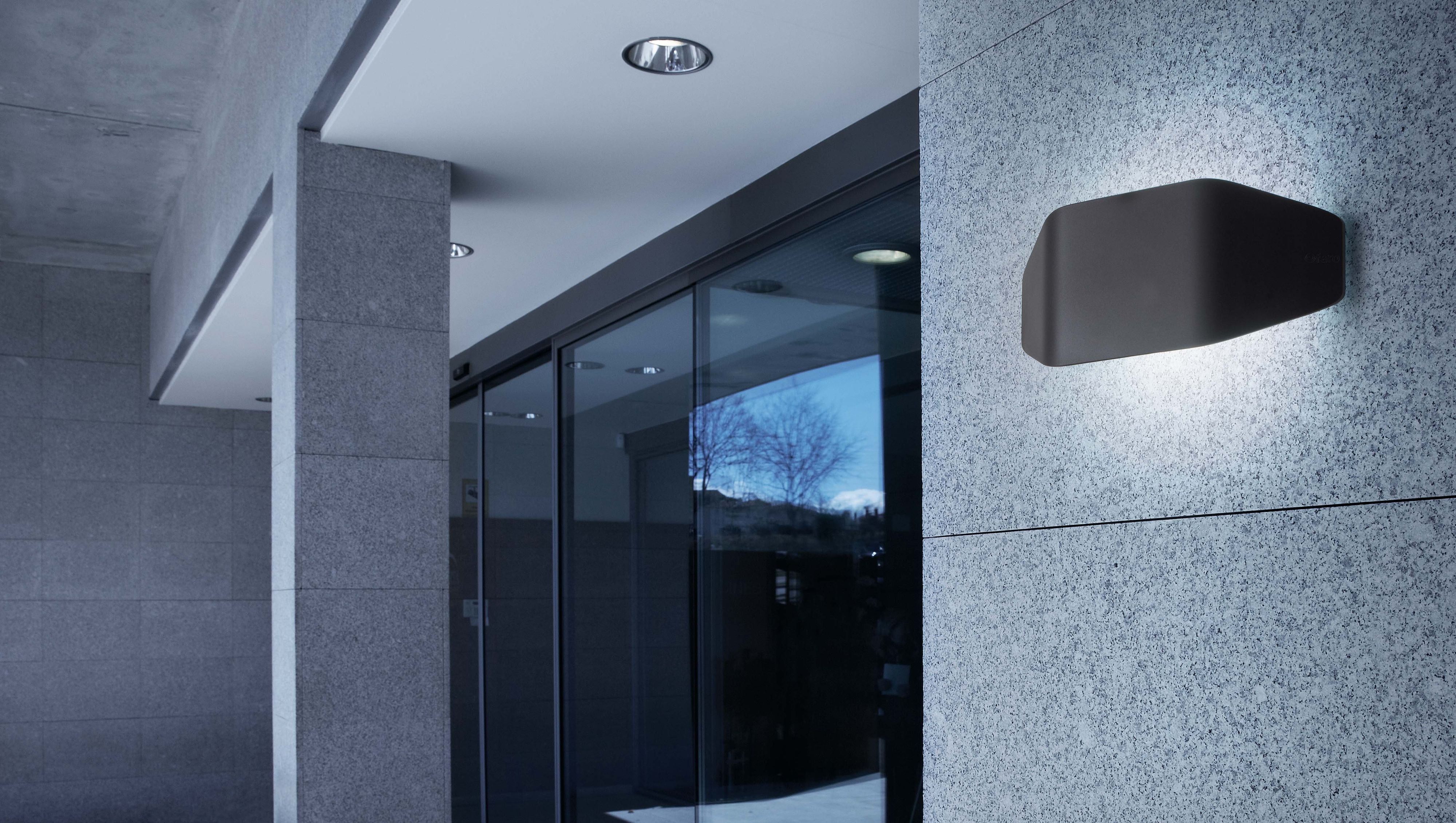 Parete esterna con un apparecchio di illuminazione scuro, rettangolare, montato a parete. Il muro è in pietra.