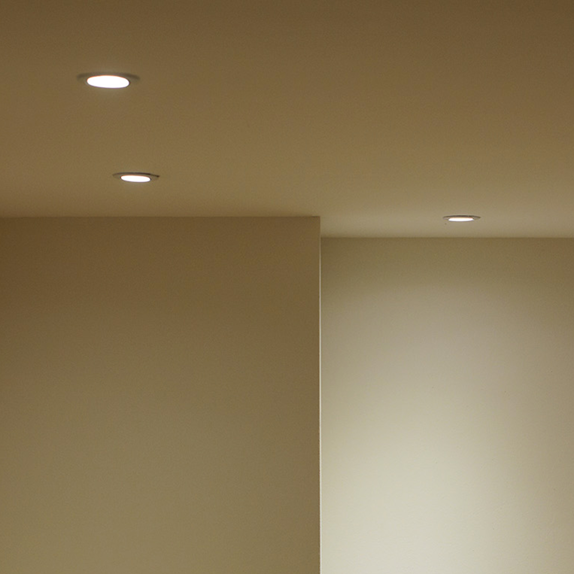 Einbaudeckenleuchten in einem beigefarbenen Raum, drei Leuchten sind sichtbar, eine Wand und die Decke.