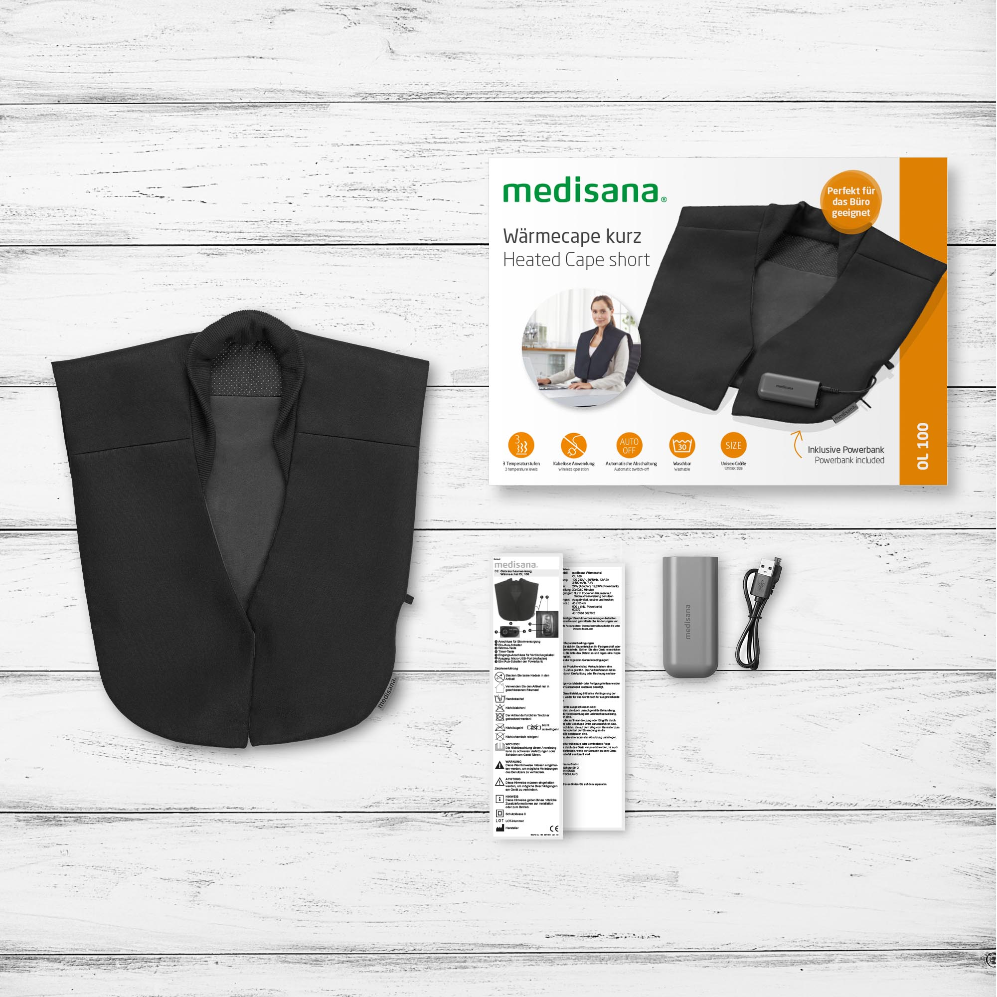 Capa calefactada negra con embalaje, incluyendo un banco de energía e instrucciones, sobre una superficie de madera.