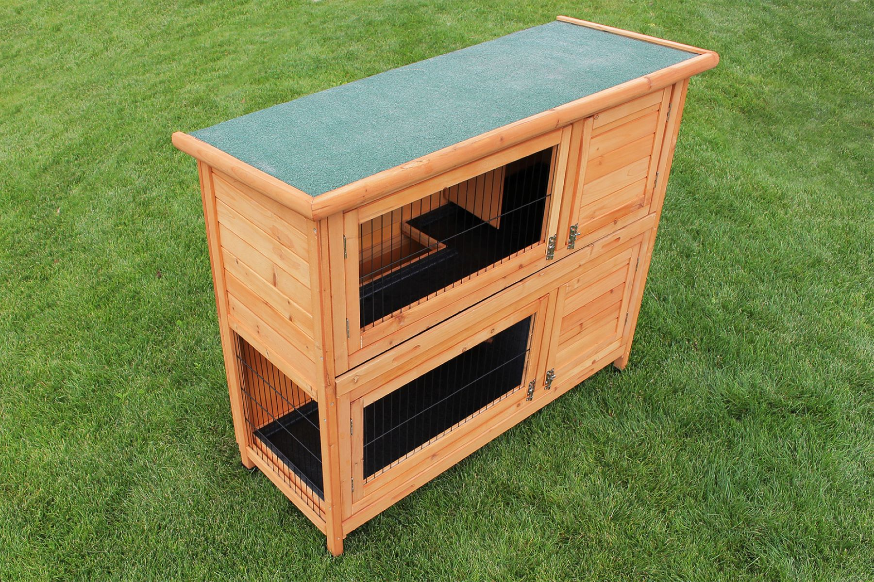 Ein Kaninchenstall aus Holz mit zwei Ebenen. Er steht auf grünem Gras.