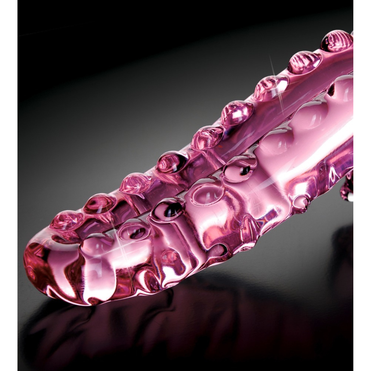 Ein pinkfarbenes, geriffeltes Sexspielzeug mit geschwungener Form, das auf einer schwarzen Oberfläche liegt. Es glänzt.