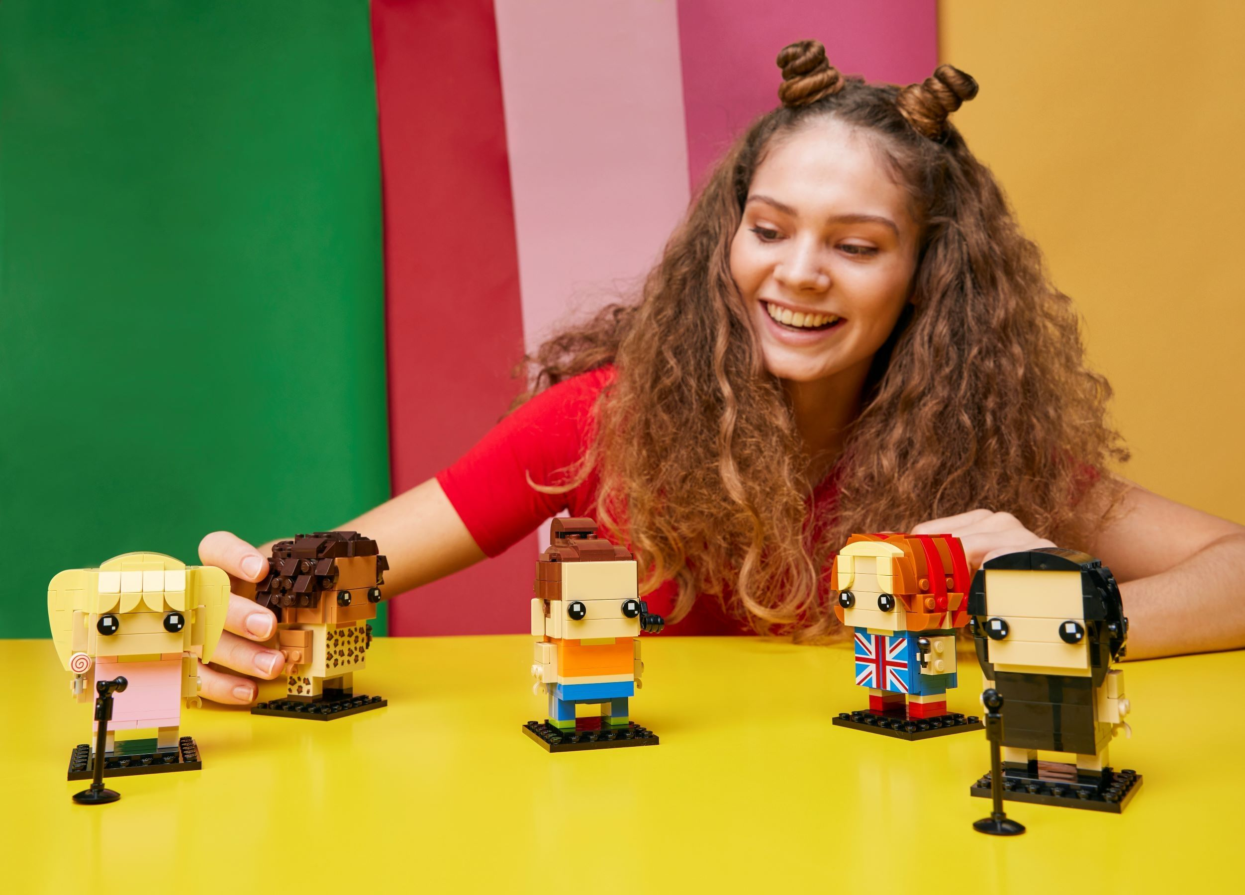 Uśmiechnięta kobieta z figurkami Lego Spice Girls na żółtej powierzchni.