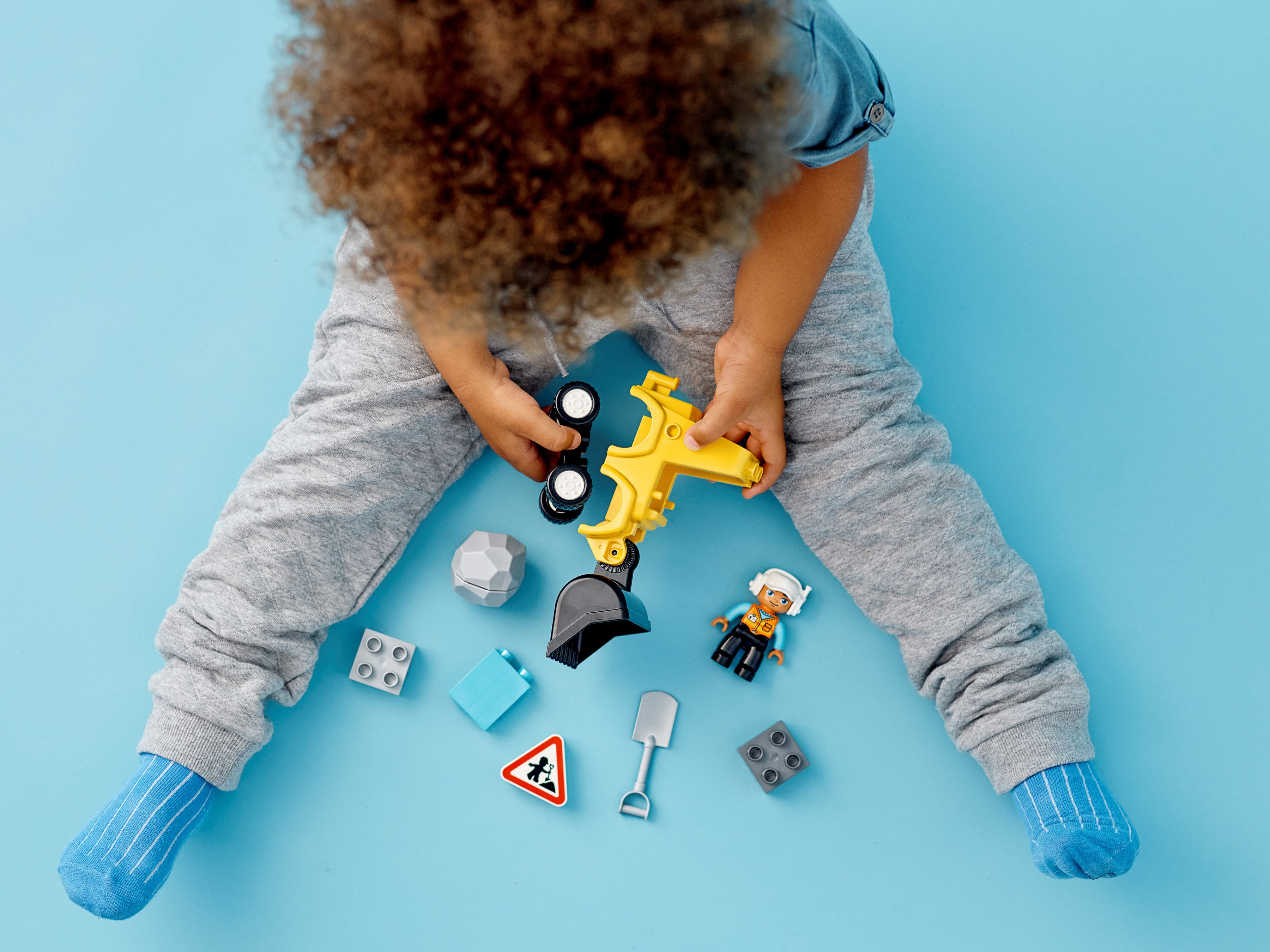 Ein Kind spielt mit Spielzeugbauelementen auf einer blauen Oberfläche, Draufsicht.