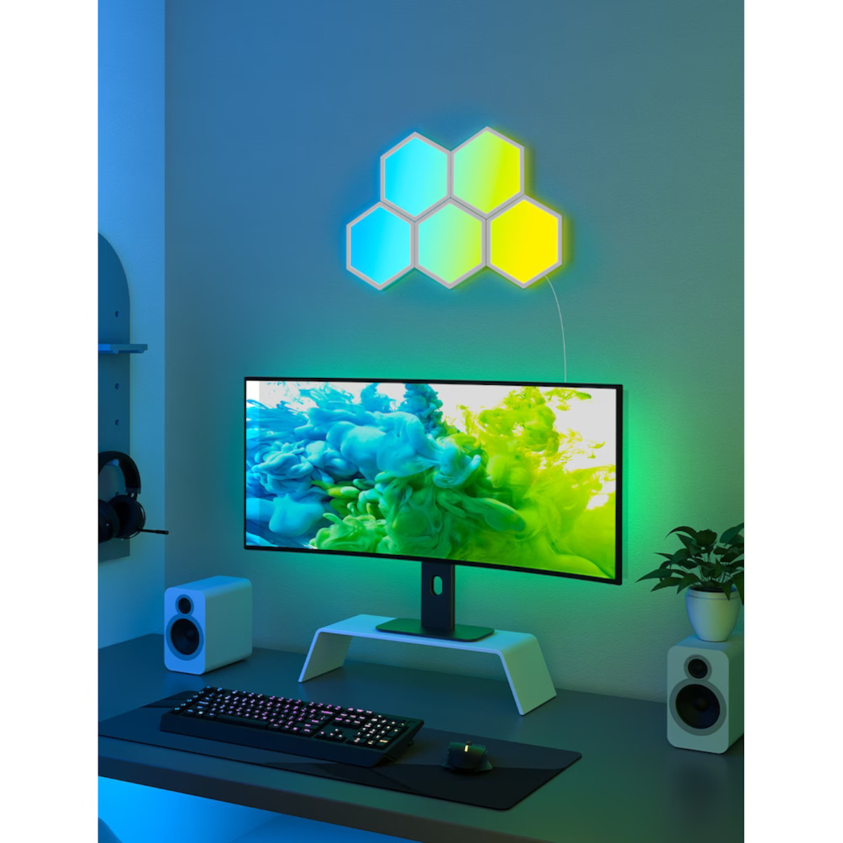 Schreibtisch mit Monitor, Tastatur, Maus und Lautsprechern. Sechseckige Lichter an der Wand.