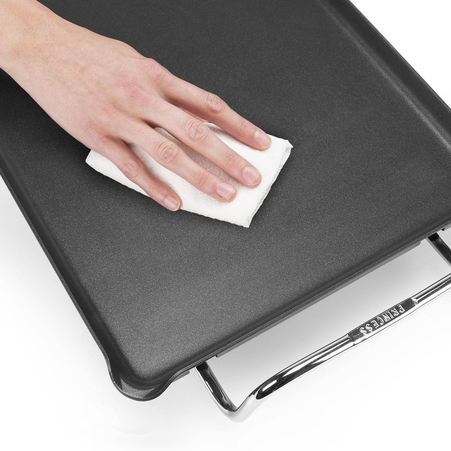 Mano limpiando una plancha negra con un paño, fondo blanco.