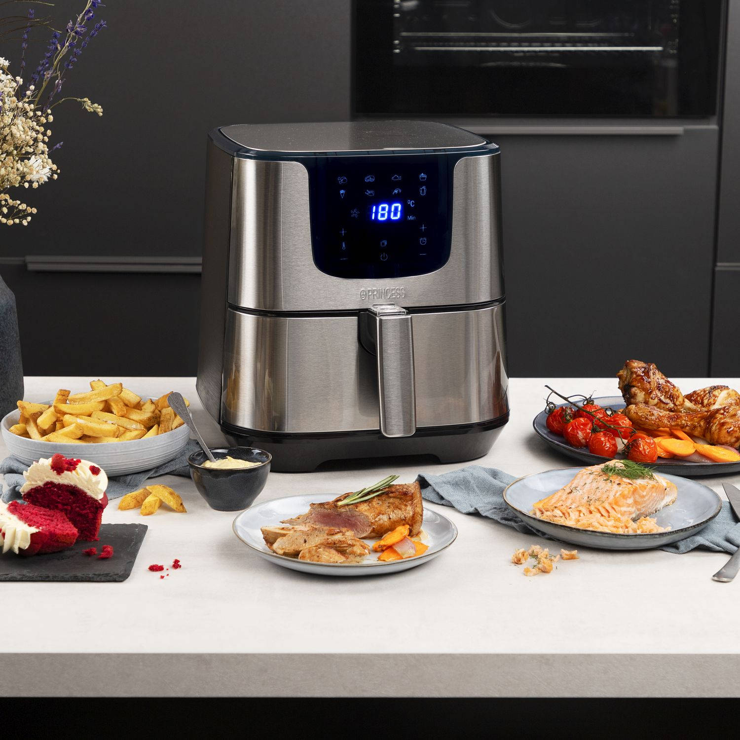 Srebrna frytkownica beztłuszczowa z jedzeniem na stole. Zawiera frytki, łososia i kurczaka.