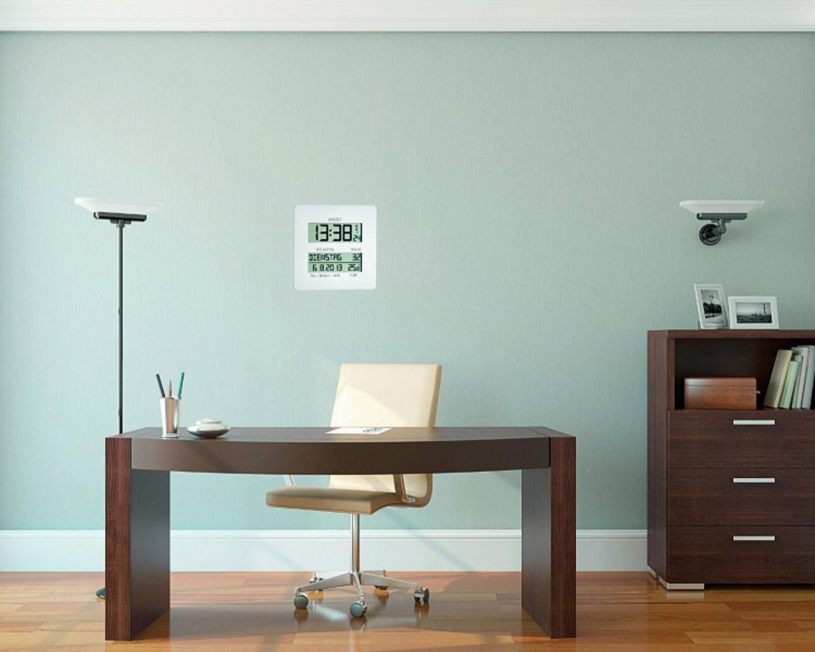 Digitaluhr an der Wand zeigt Zeit und Datum, neben Schreibtisch und Schrank.