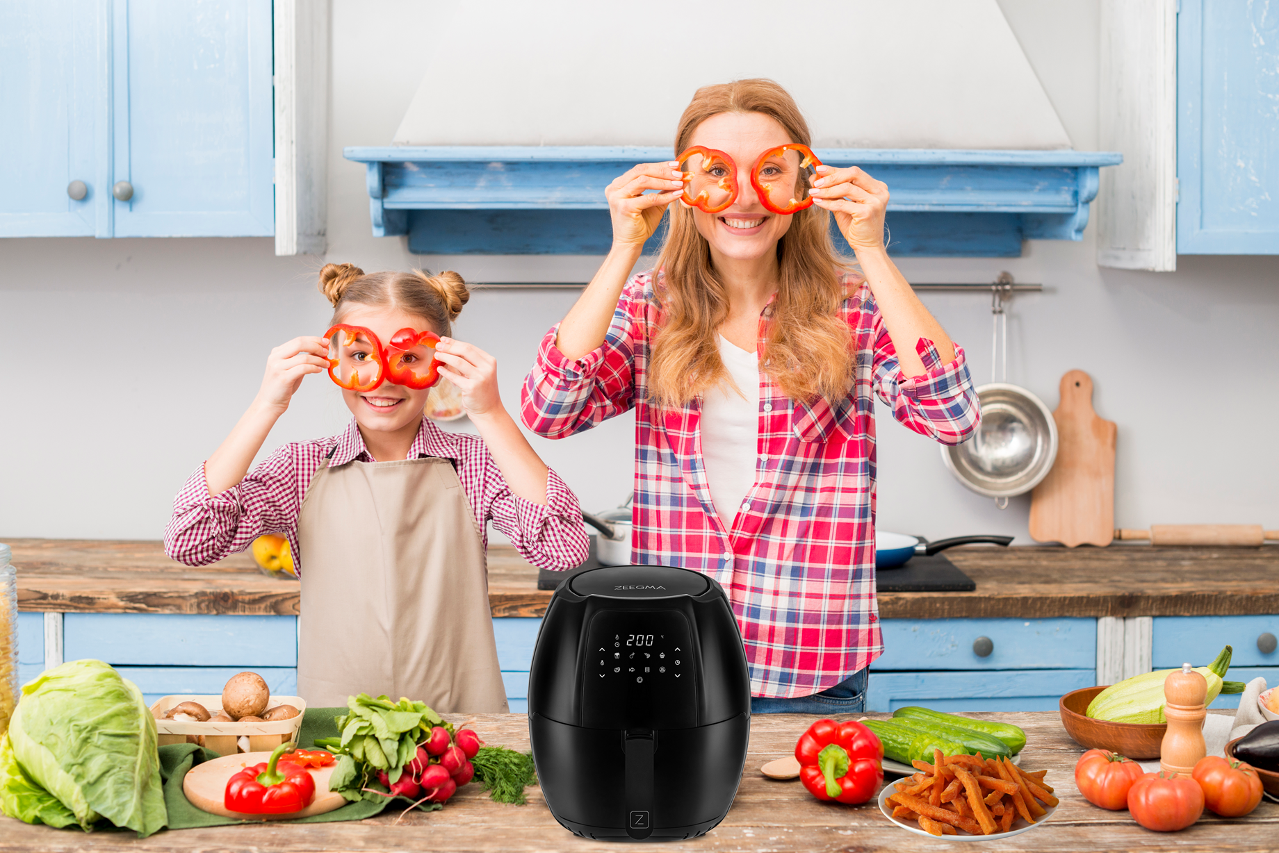 Matka i córka trzymają paprykę. Czarna frytkownica beztłuszczowa jest na pierwszym planie.