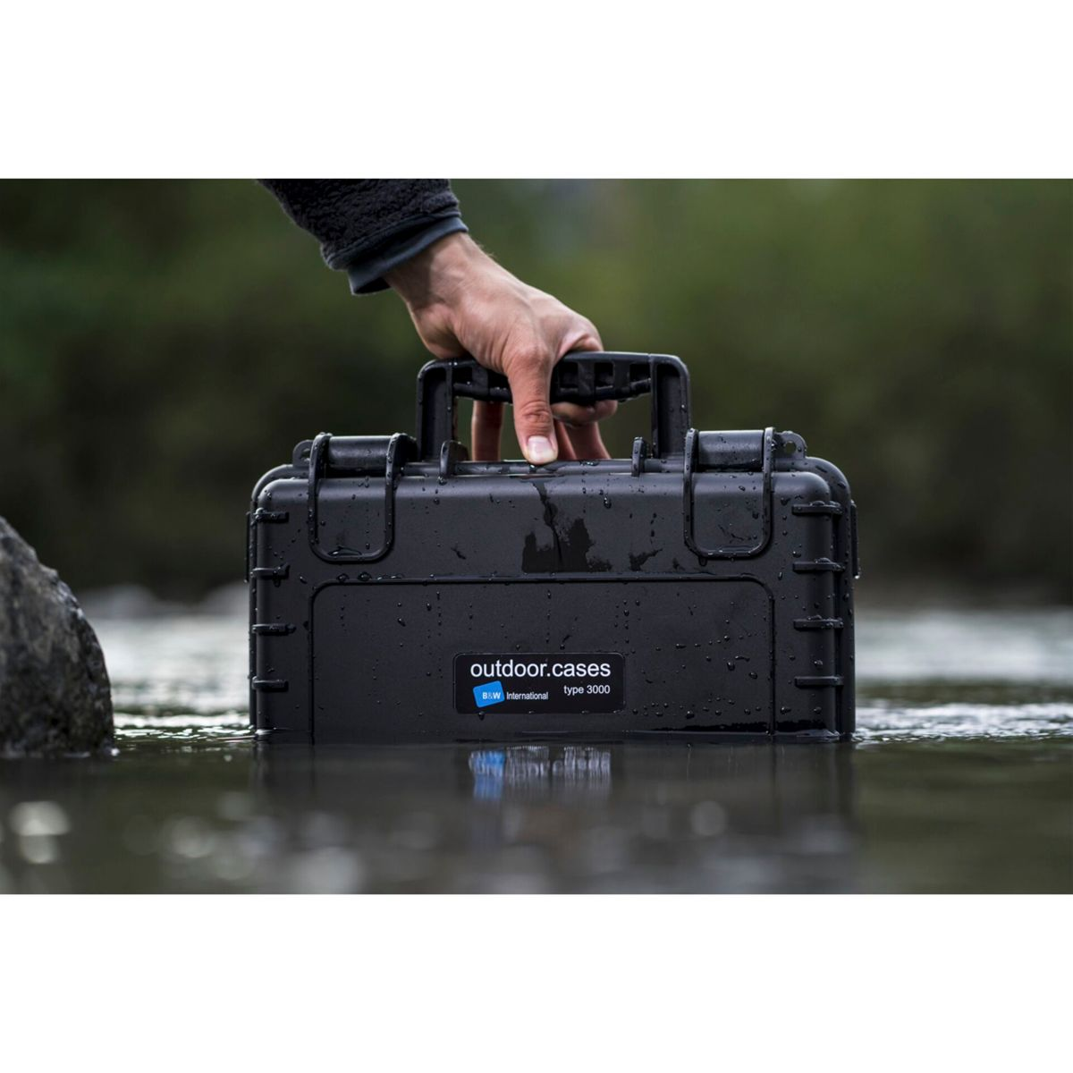 Eine schwarze Kiste im Wasser, gehalten von einer Hand. Die Kiste hat ein Etikett.