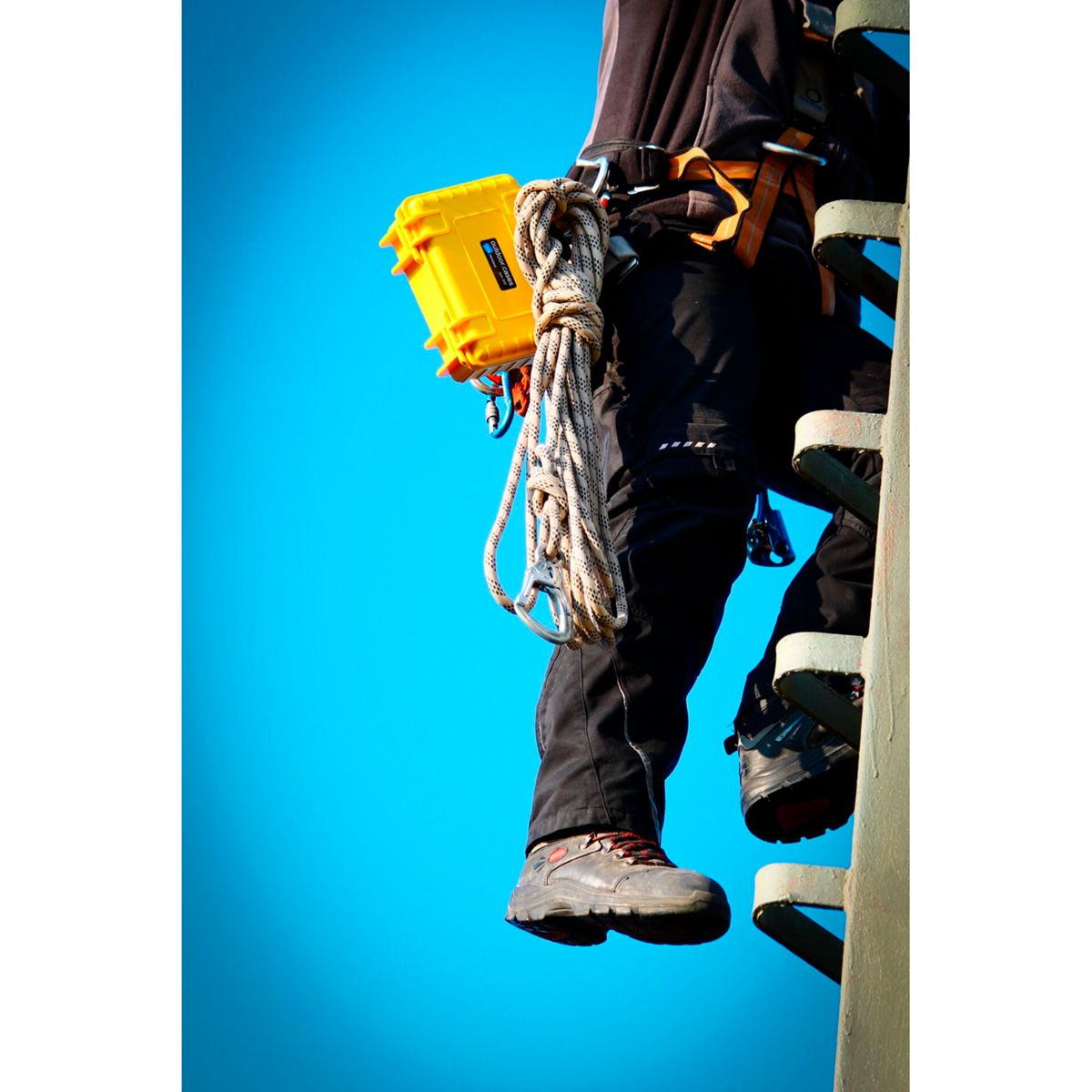 Eine Person auf einem Turm, mit einer gelben Box und einem Seil. Beine und Stiefel sind sichtbar.
