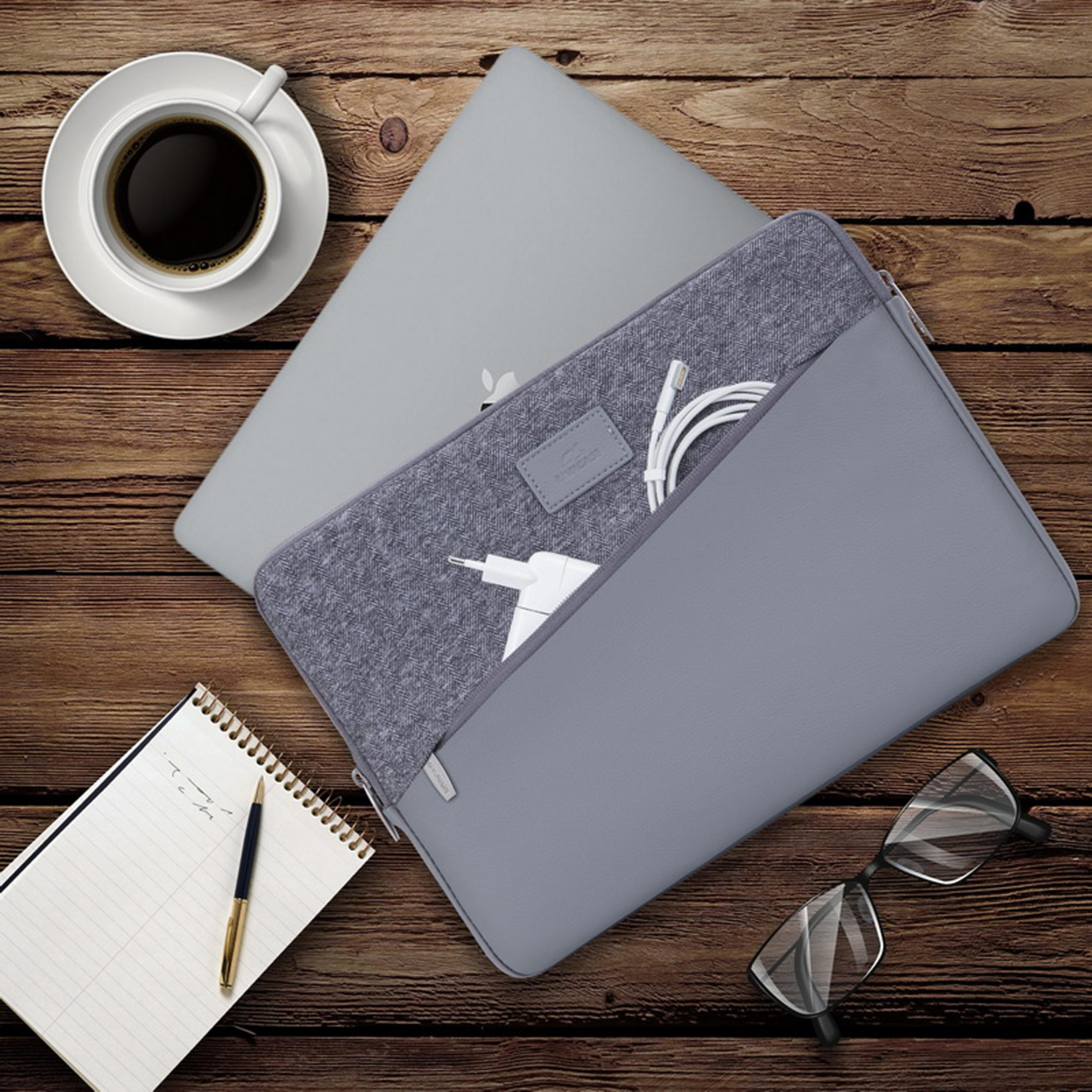 Laptop, custodia grigia e accessori su un tavolo di legno. Include caffè, blocco note, occhiali e caricabatterie.