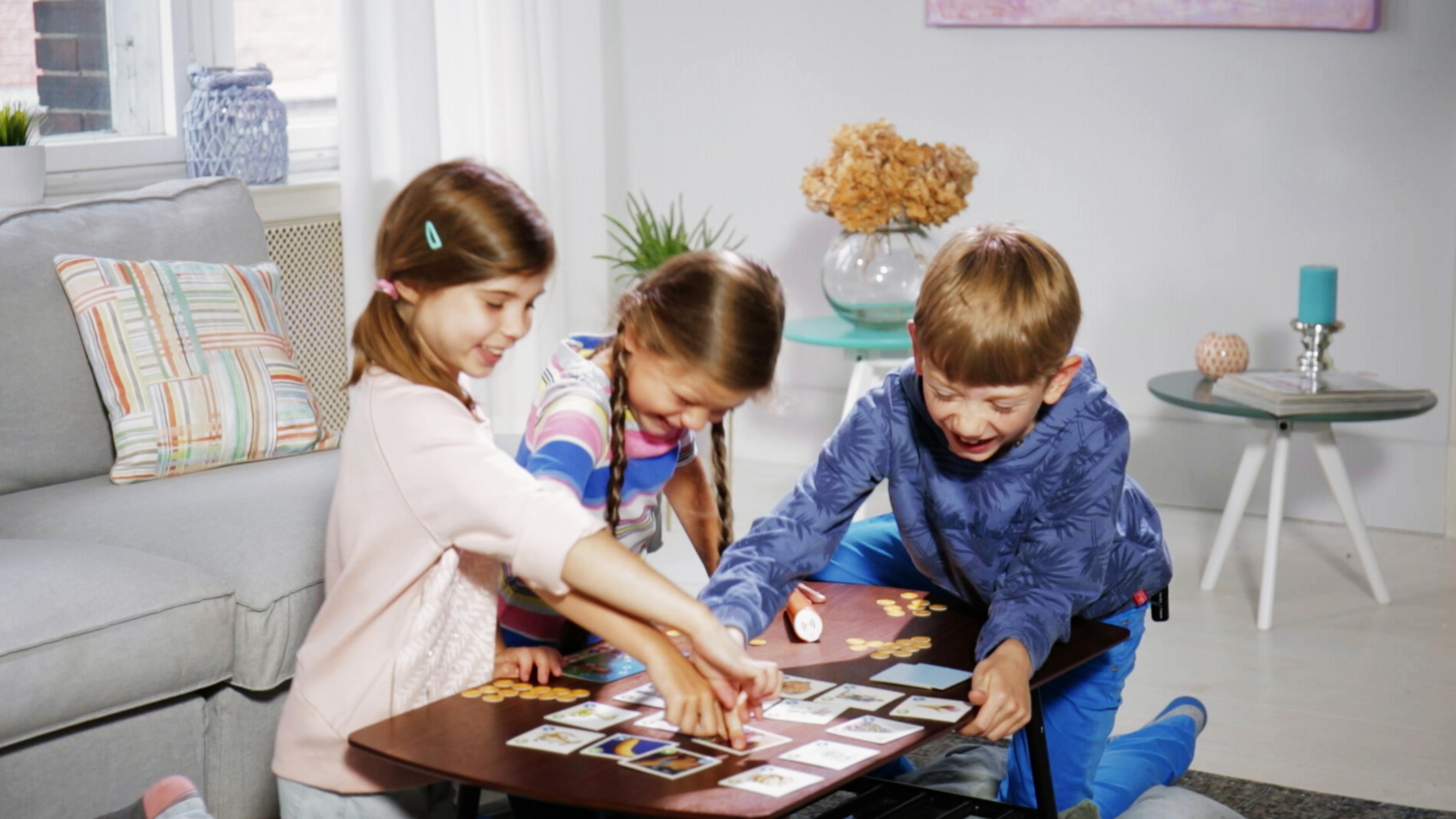 Drei Kinder spielen ein Brettspiel. Sie sitzen um einen kleinen Tisch.