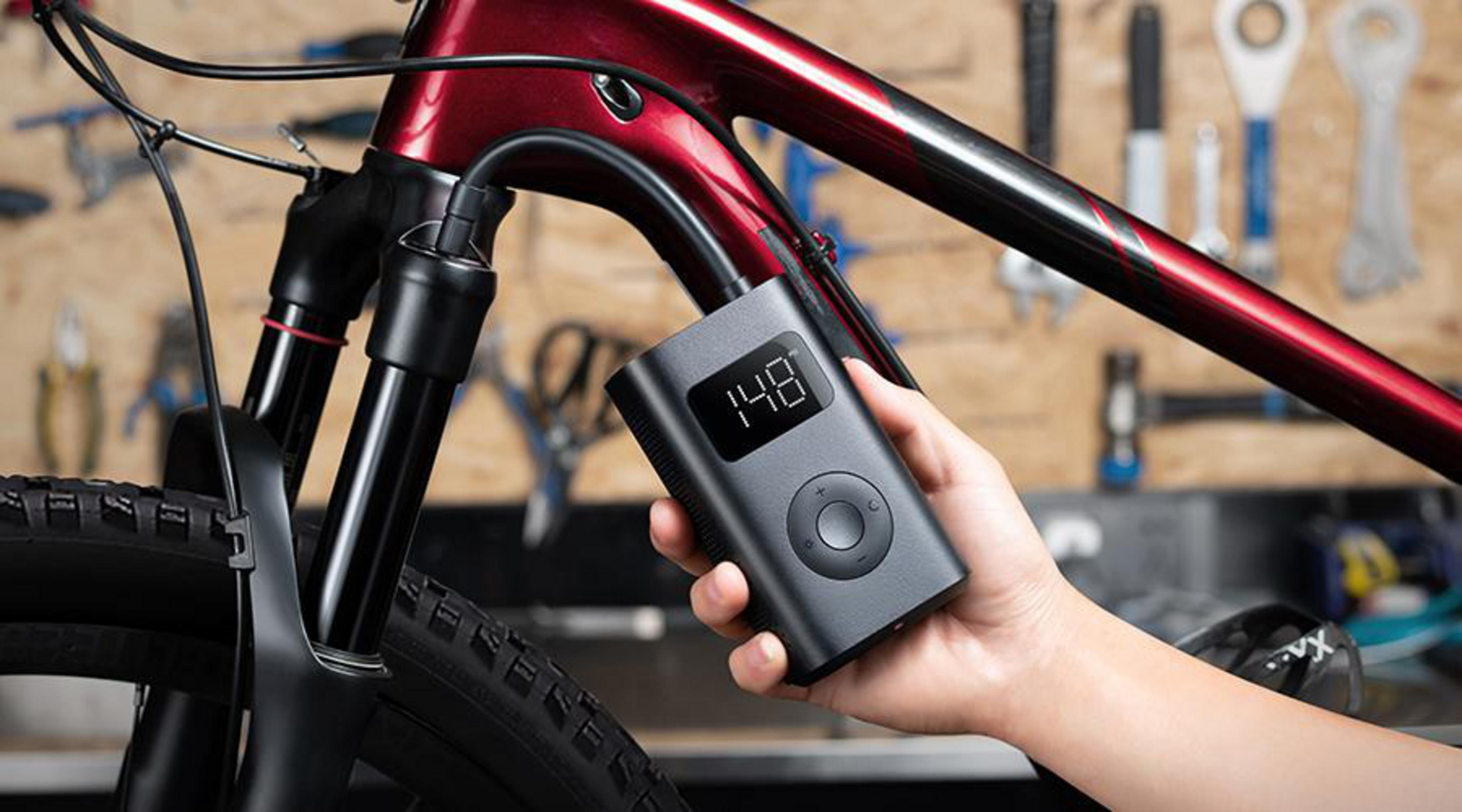 Een hand die een zwarte luchtpomp vasthoudt naast een fiets. Het display toont '148'.