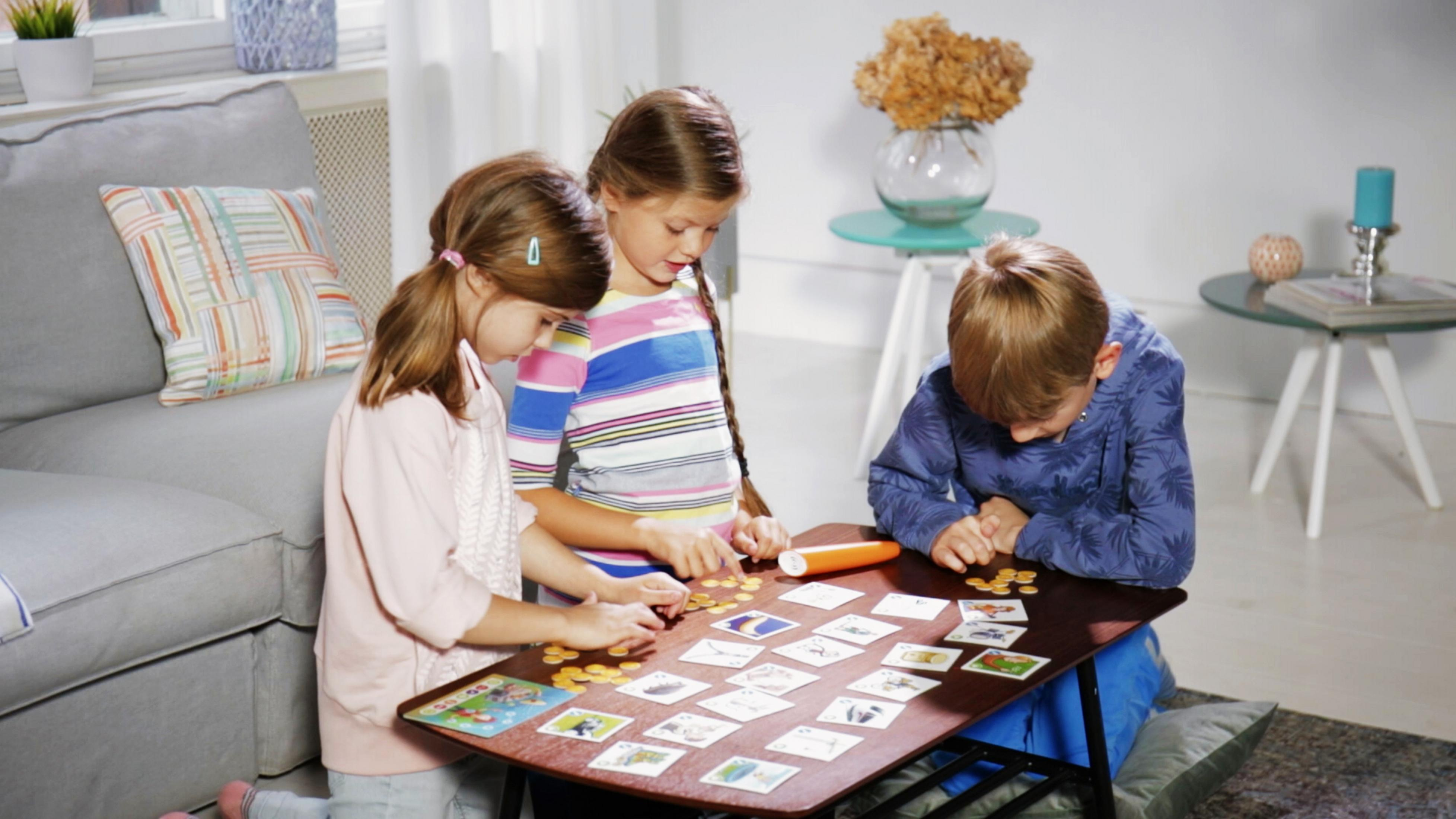 Drei Kinder spielen ein Brettspiel. Sie konzentrieren sich auf das Spiel. Der Raum ist hell.