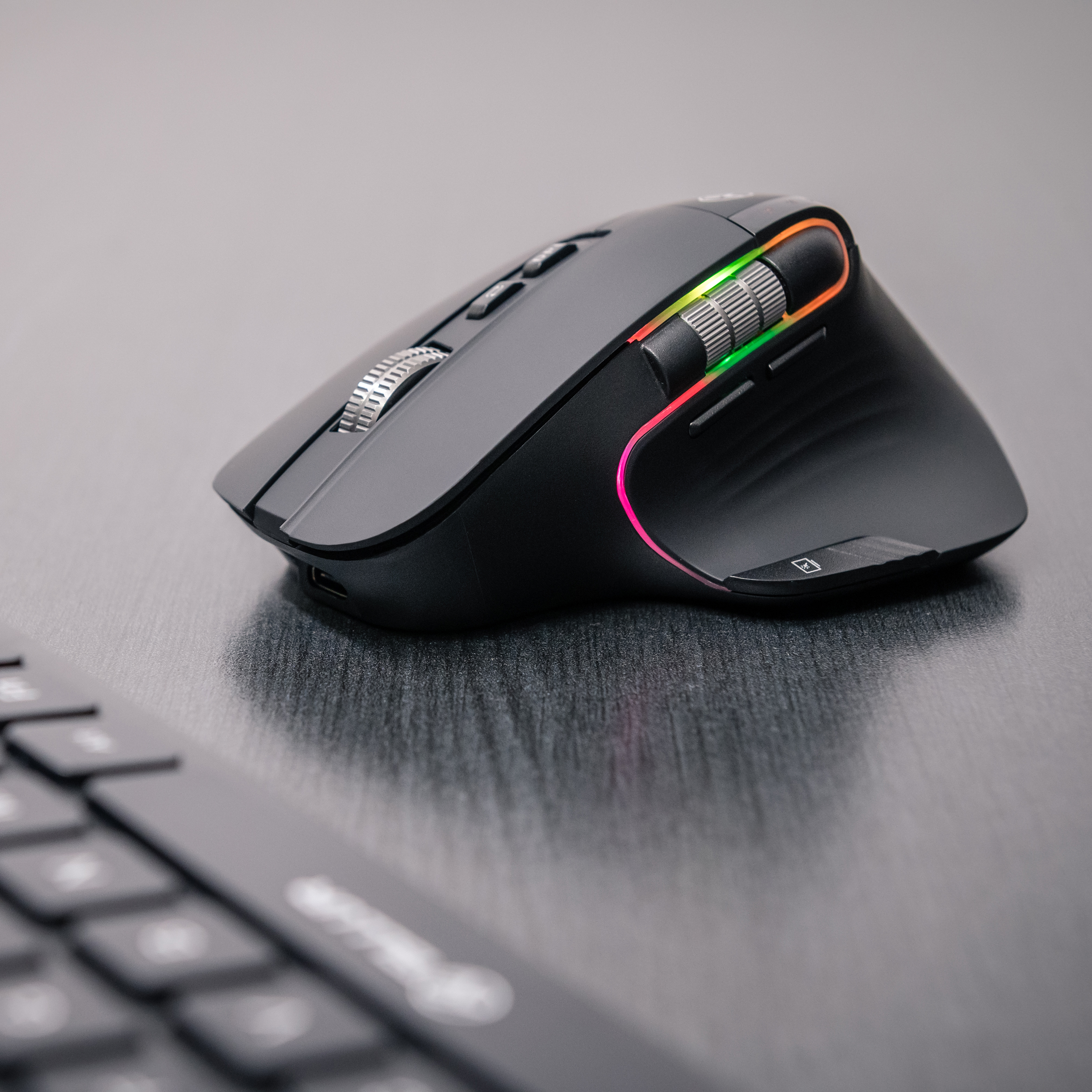 Czarna mysz komputerowa z kolorowymi światłami i rolkami na biurku.