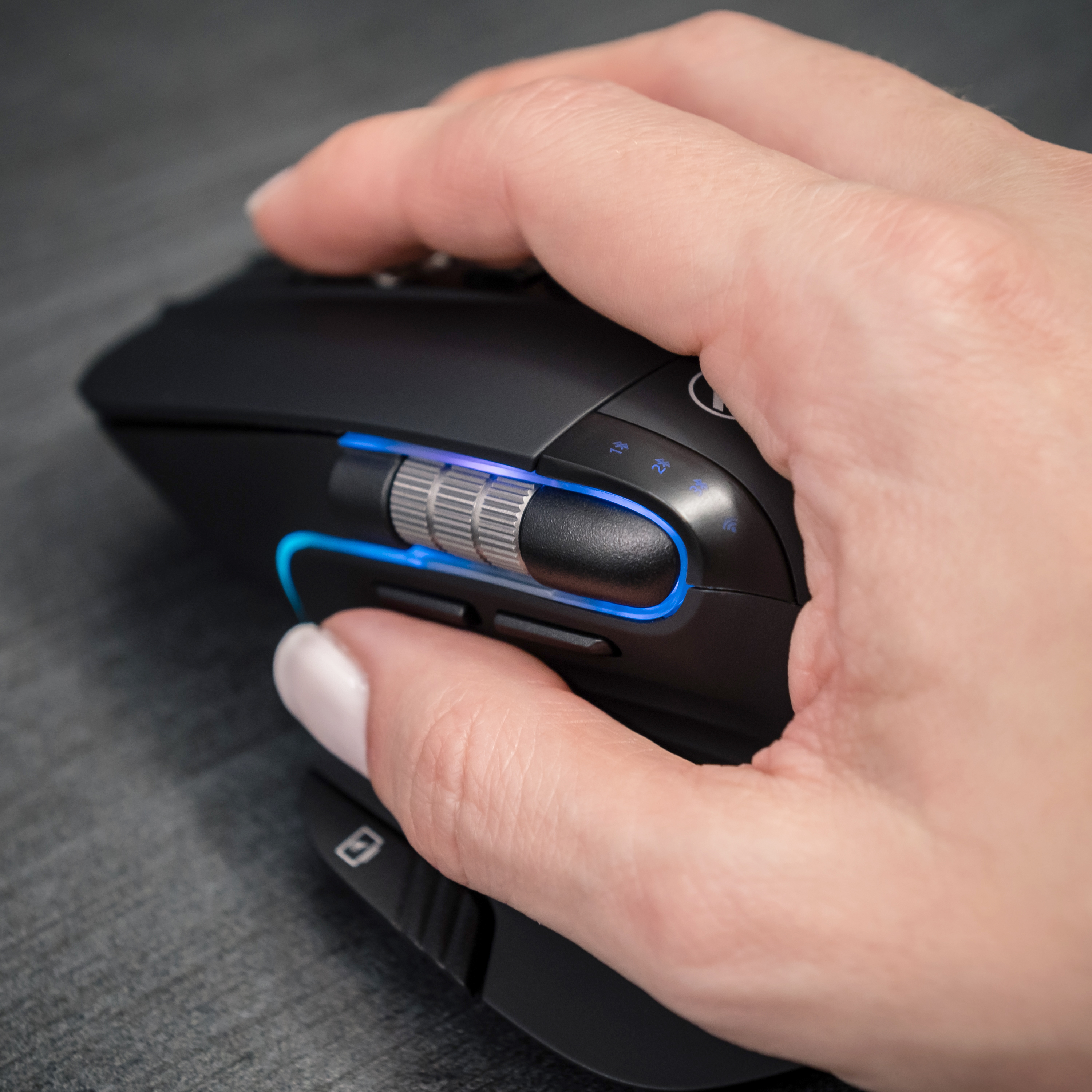 Dłoń trzymająca czarną mysz komputerową z niebieskim światłem.