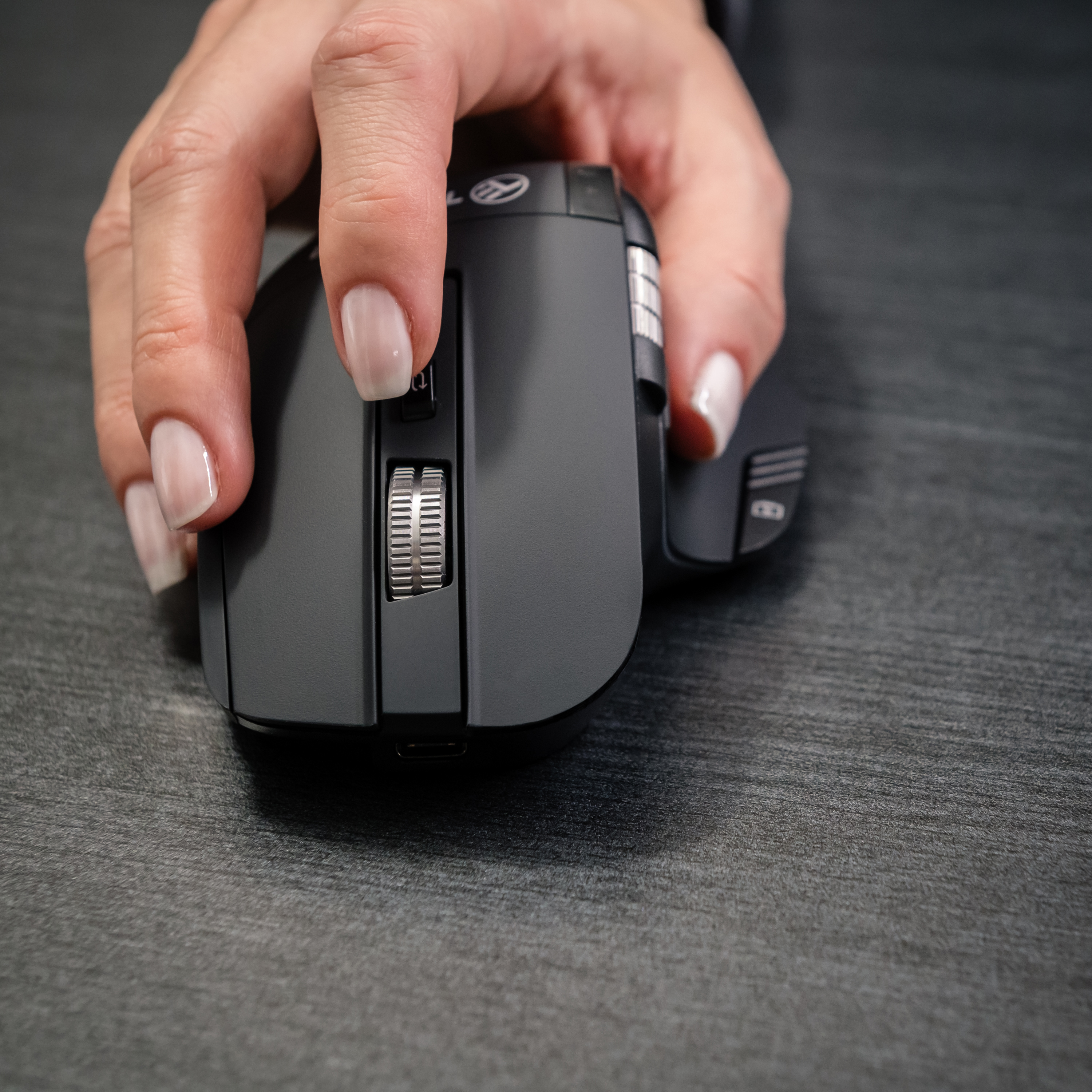 Dłoń obsługująca czarną mysz. Mysz znajduje się na ciemnej powierzchni.