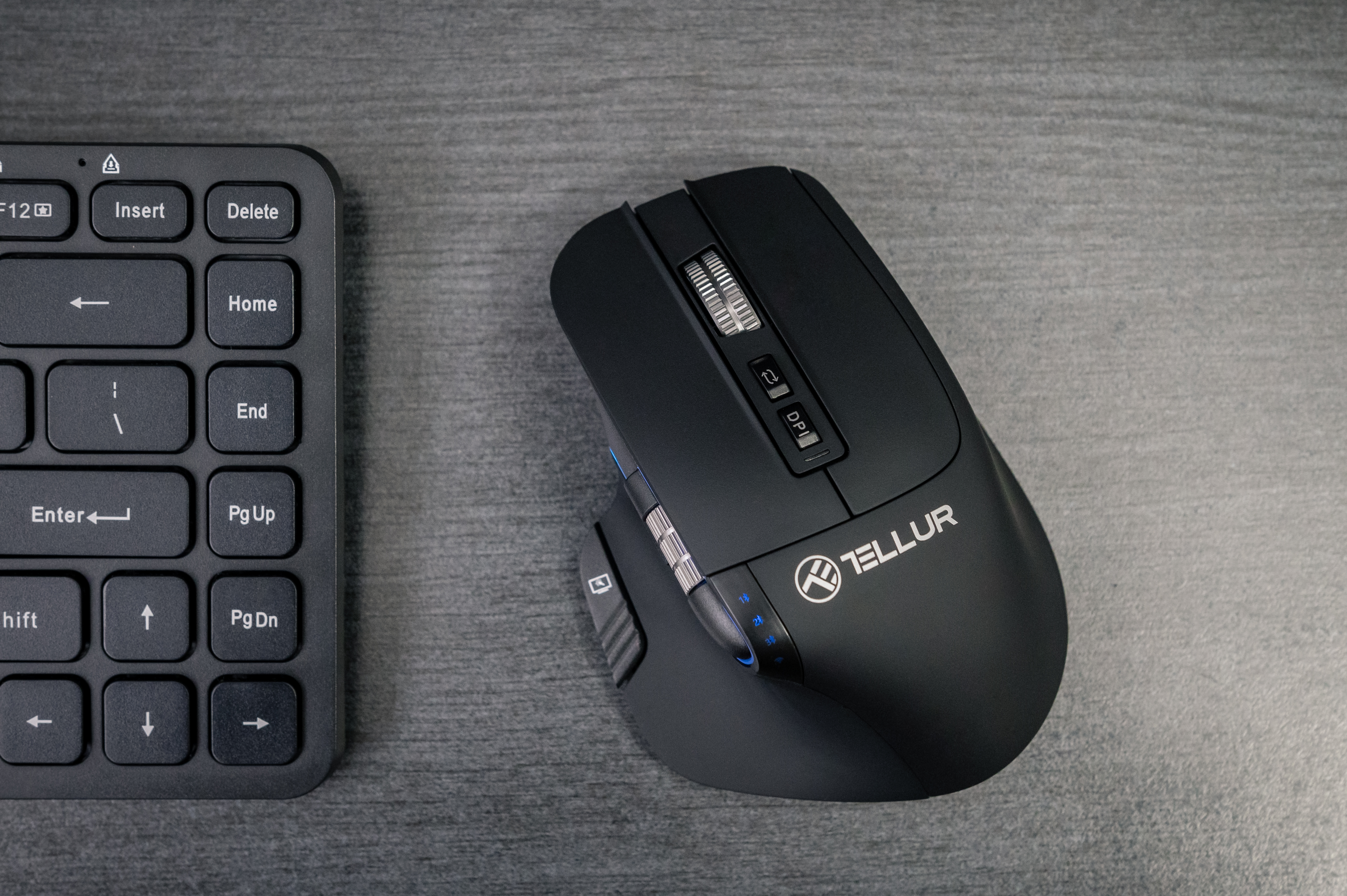 Czarna mysz i klawiatura na szarej powierzchni. Myszka ma logo Tellur i przyciski. Klawiatura jest minimalistyczna.