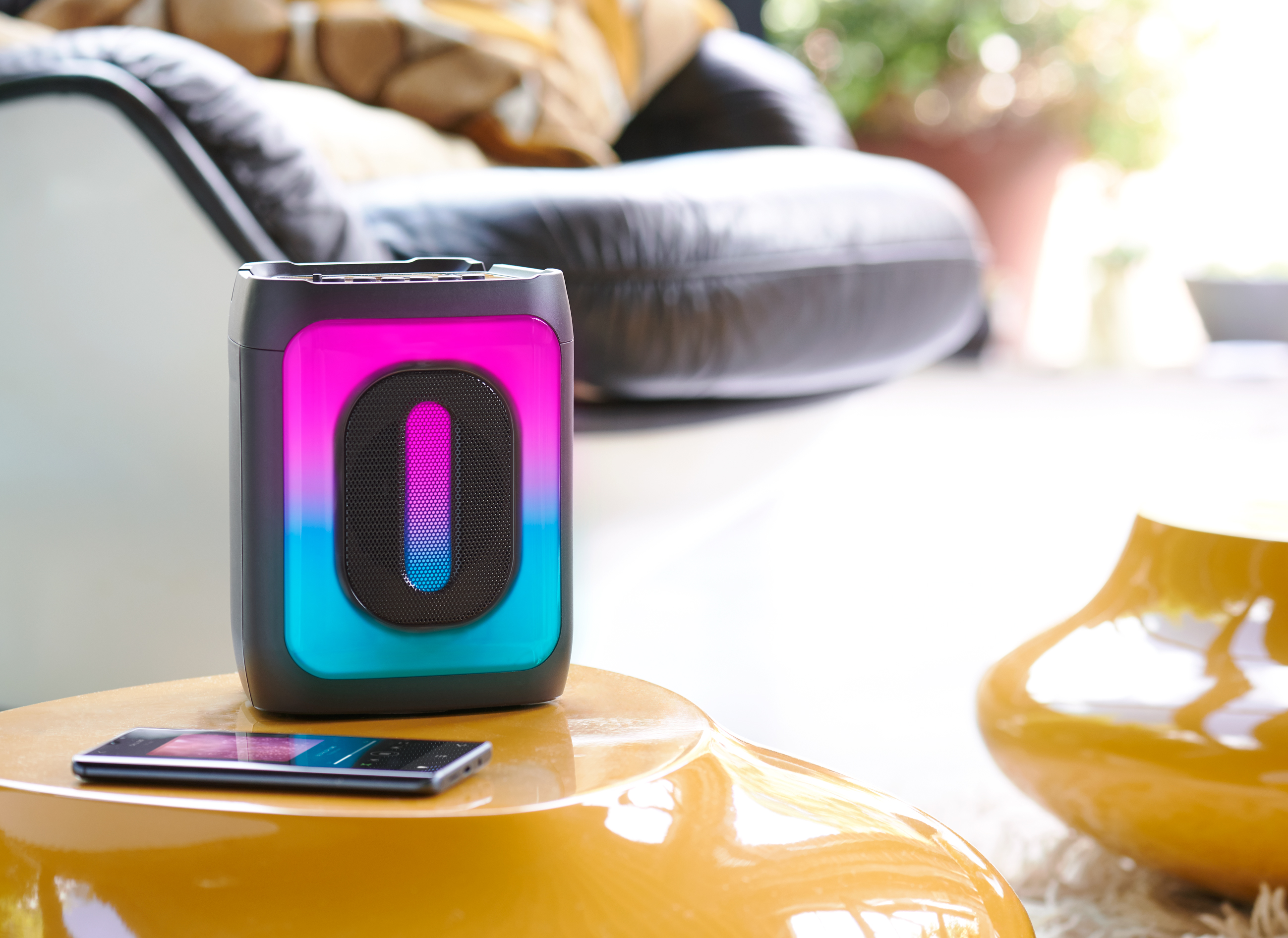Przenośny głośnik z kolorowym panelem świetlnym, obok smartfona na stole.