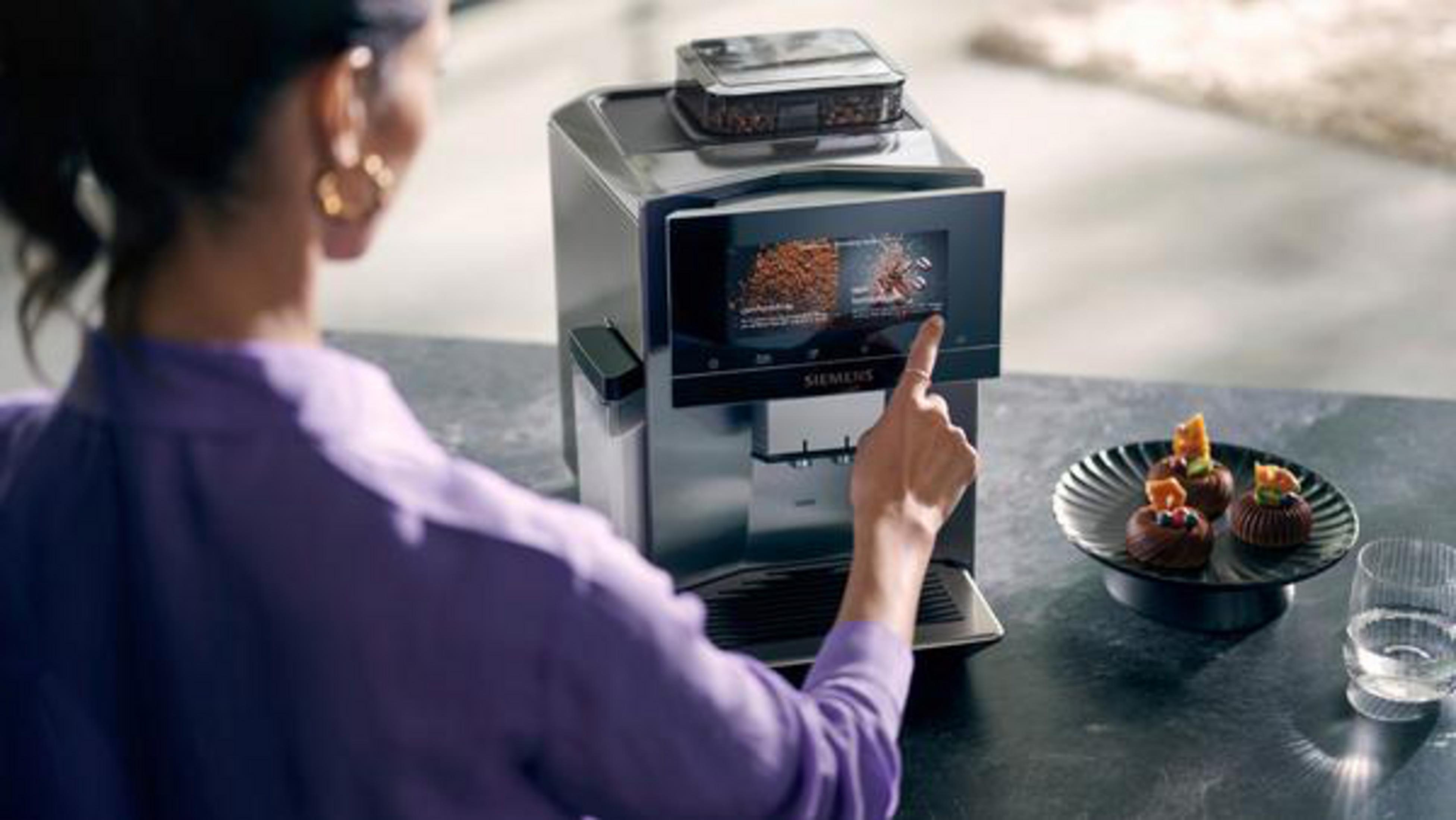 Die Hand einer Person berührt den Bildschirm einer Kaffeemaschine, Kaffee und Gebäck in der Nähe.