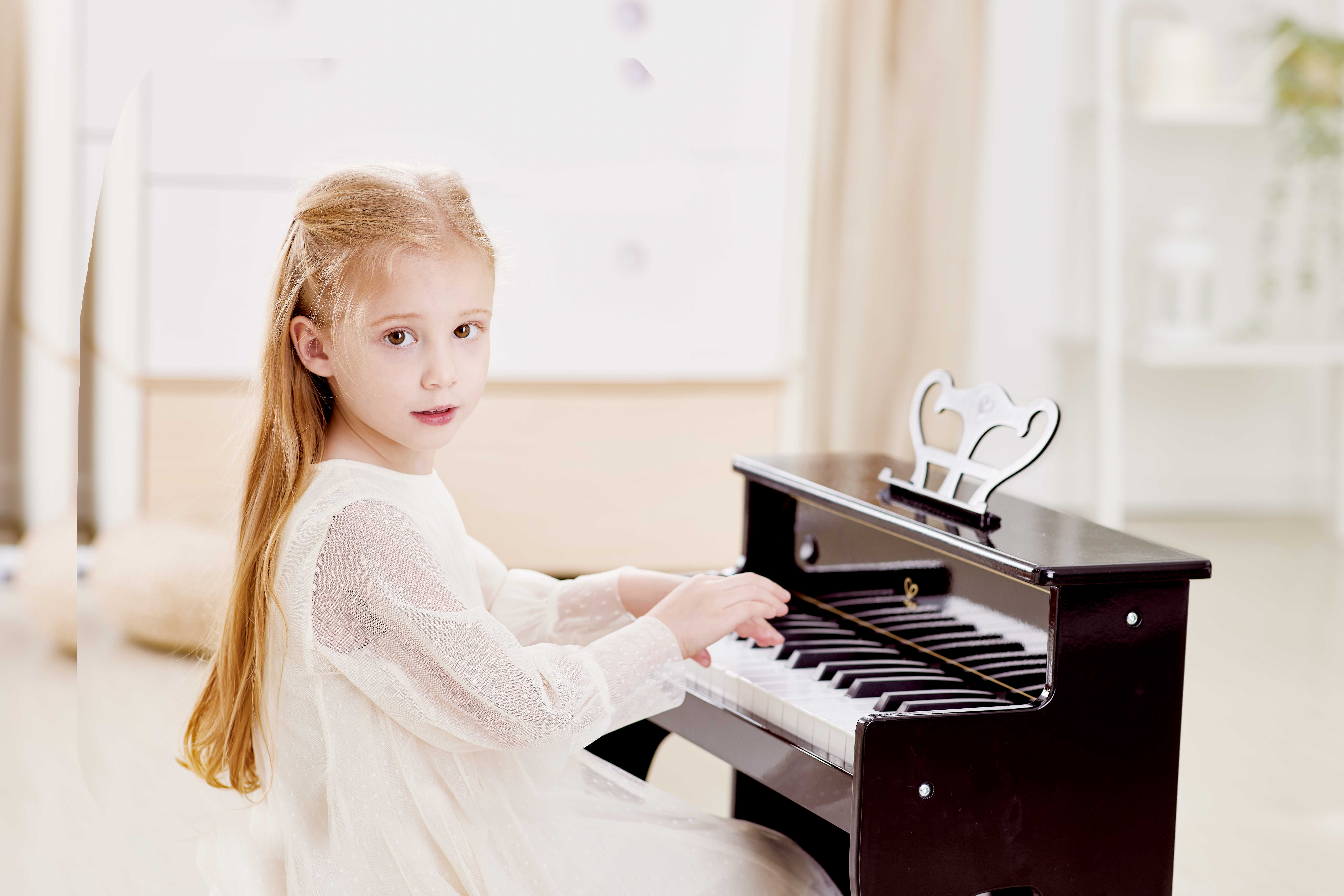 Ein junges Mädchen spielt ein kleines Klavier. Sie schaut in die Kamera.