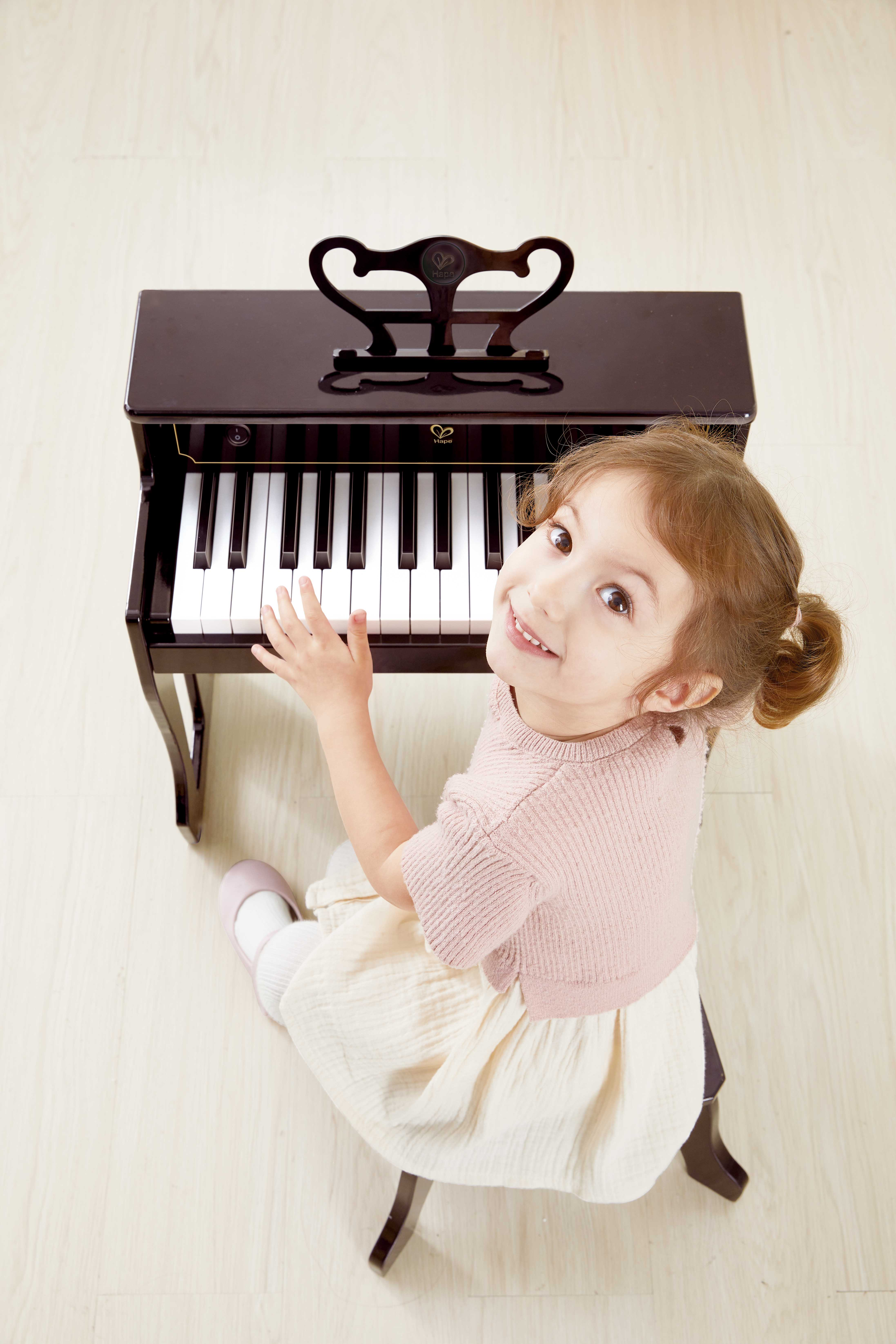 Mädchen spielt Klavier, lächelt. Braunes Klavier, weißer Hintergrund.