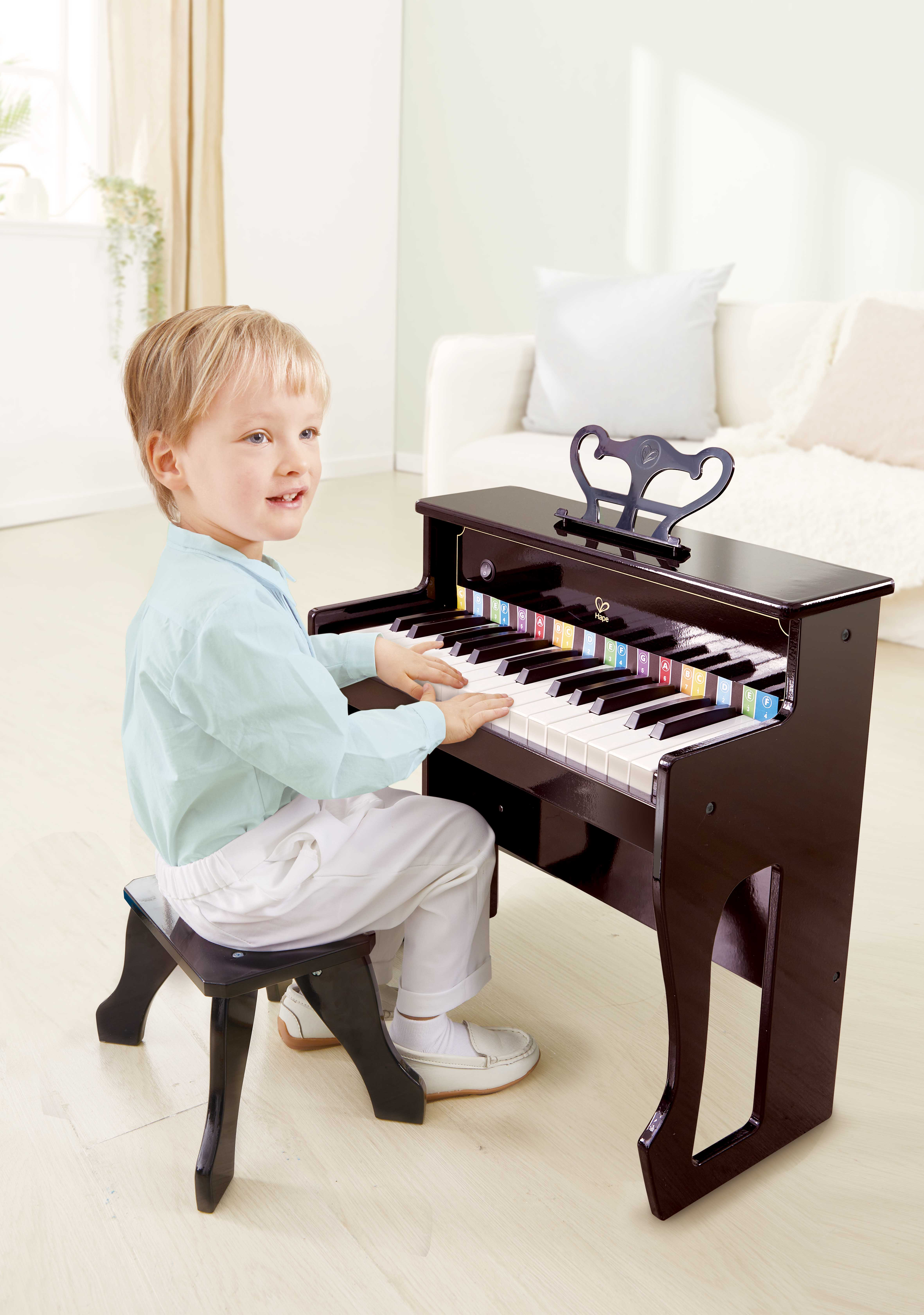 Junge spielt ein schwarzes Klavier. Er lächelt und schaut in die Kamera.