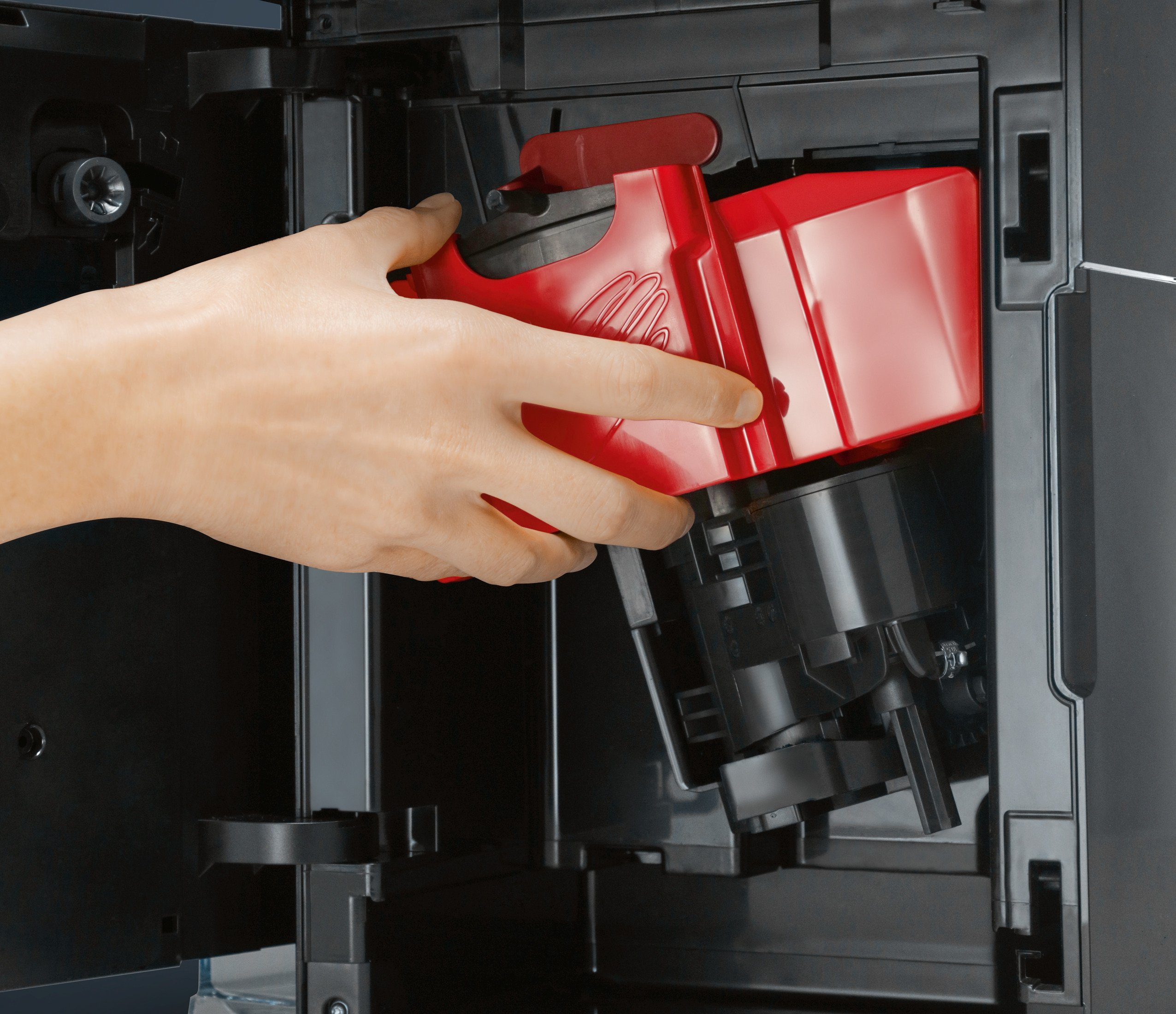Eine Hand, die einen roten Behälter aus einer schwarzen Kaffeemaschine entfernt.