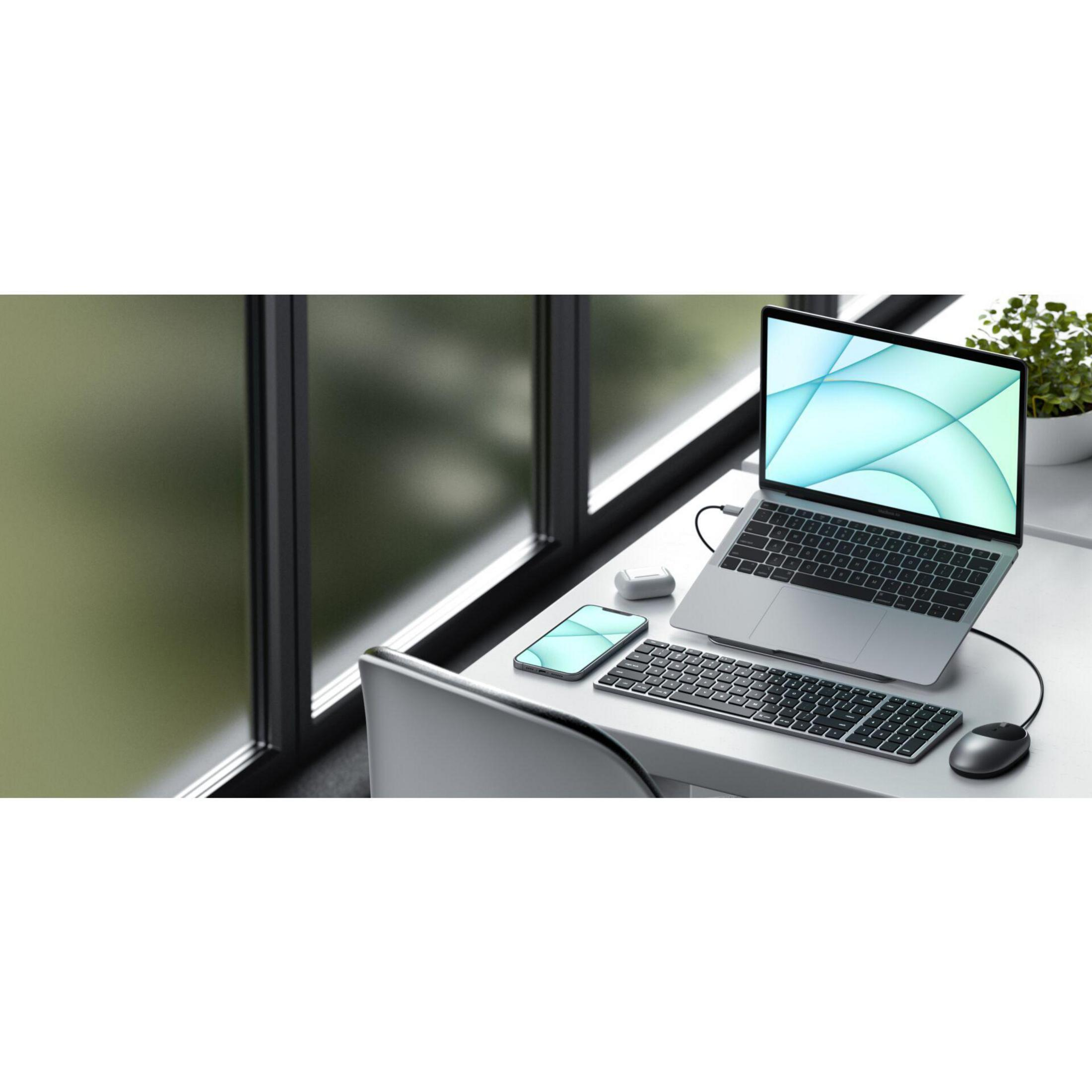 Ein Laptop, ein Telefon und eine Tastatur auf einem Schreibtisch. Der Laptop ist geöffnet. Links ist ein Fenster.