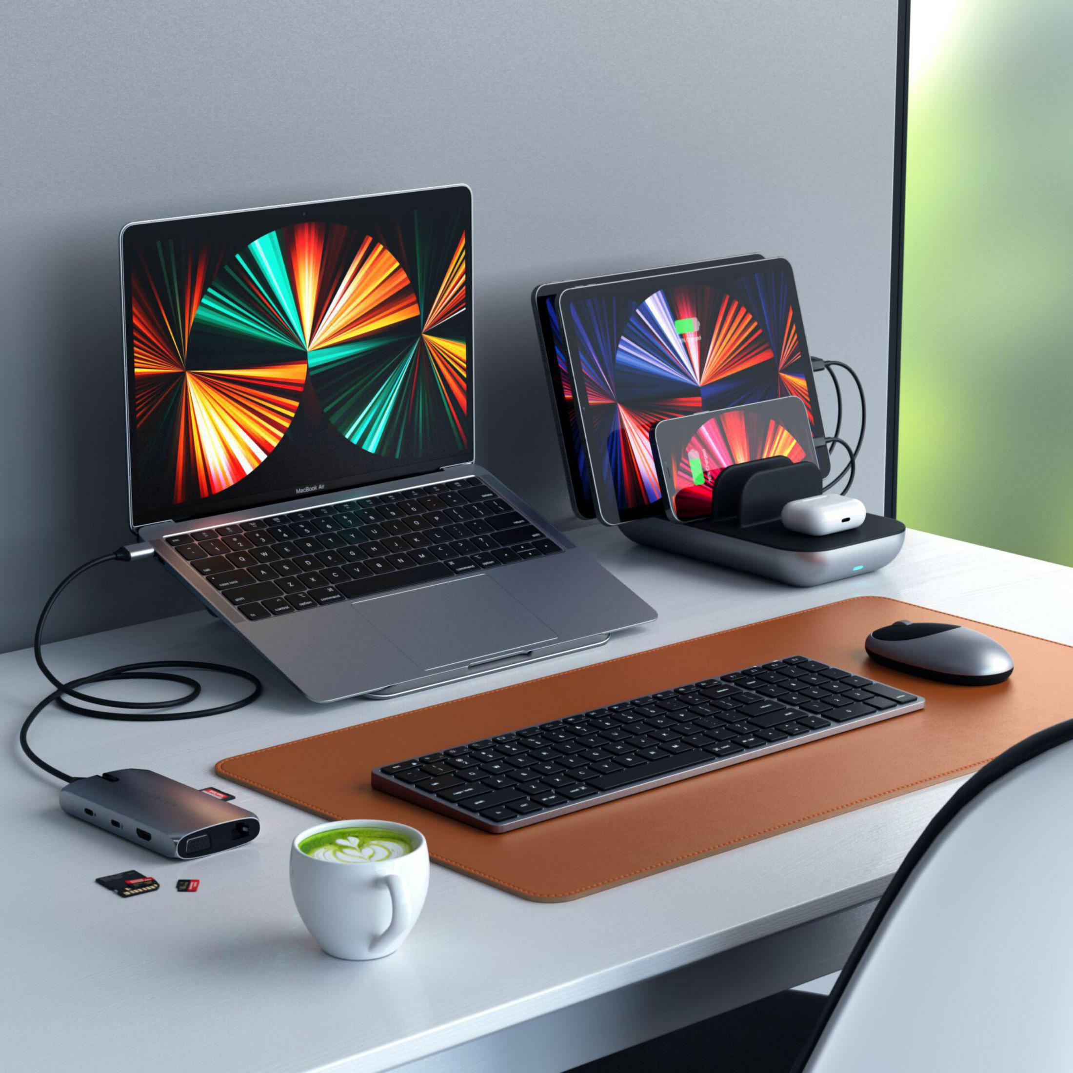 Arbeitsplatz mit Laptop, Tablet, Ladestation, Tastatur, Maus, Kaffee und Zubehör.