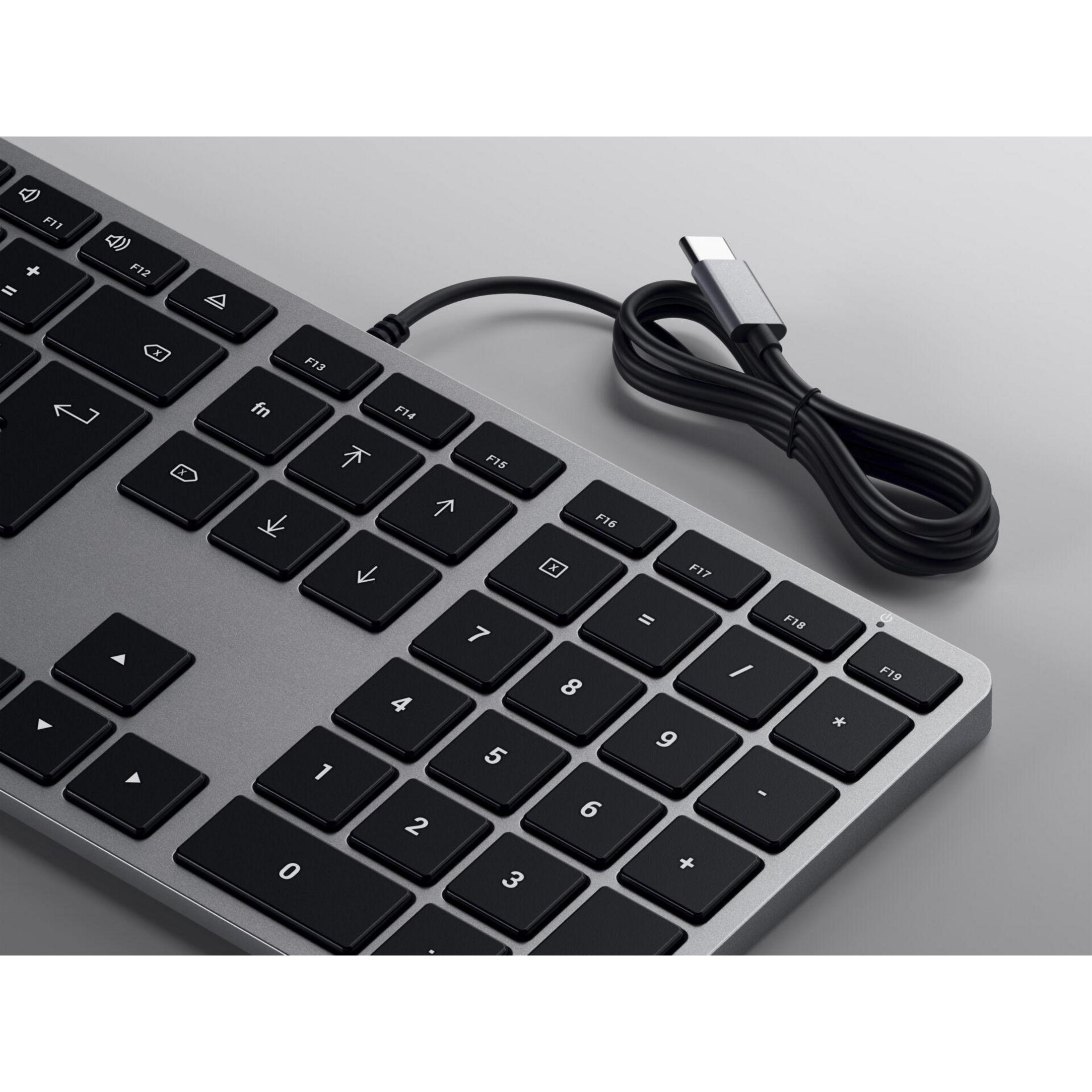 Primo piano di una tastiera argentata con tasti neri e un cavo USB-C. Superficie grigia.