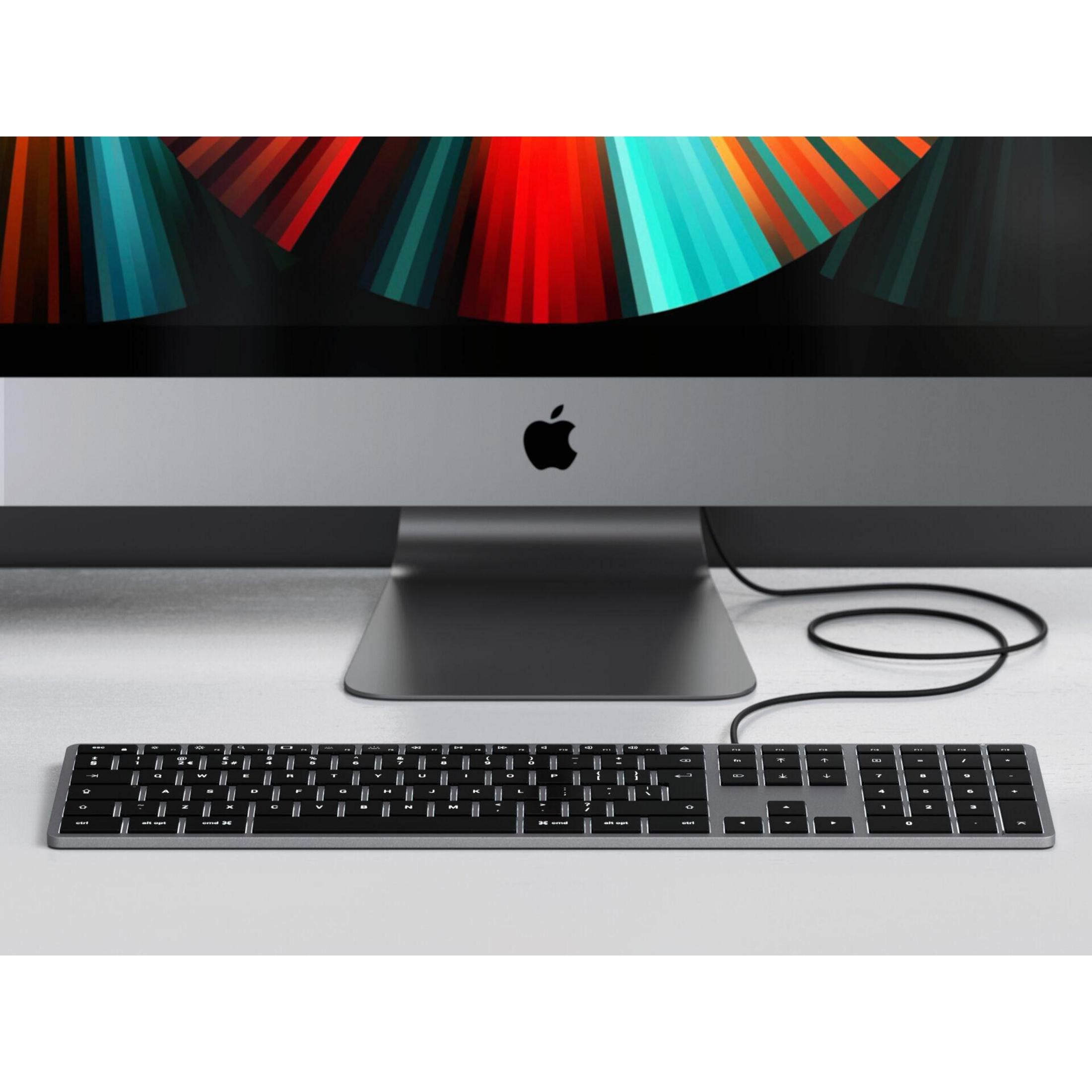 Tastiera argentata su una superficie bianca, collegata a un monitor che mostra arte astratta colorata.
