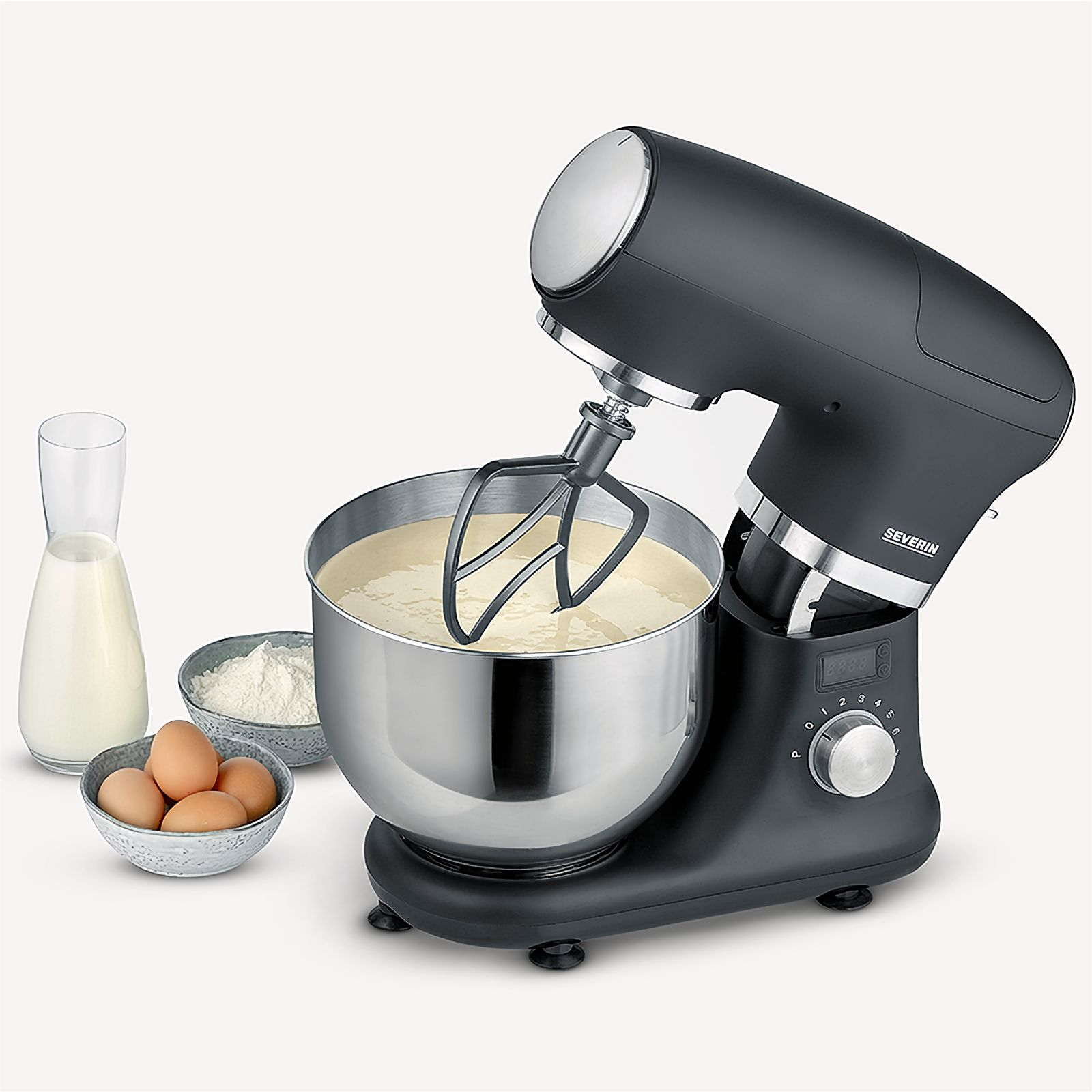 Schwarzer Küchenmixer mit einer Schüssel Teig, Zutaten in der Nähe. Ein Glas Milch, Mehl und Eier sind vorhanden.